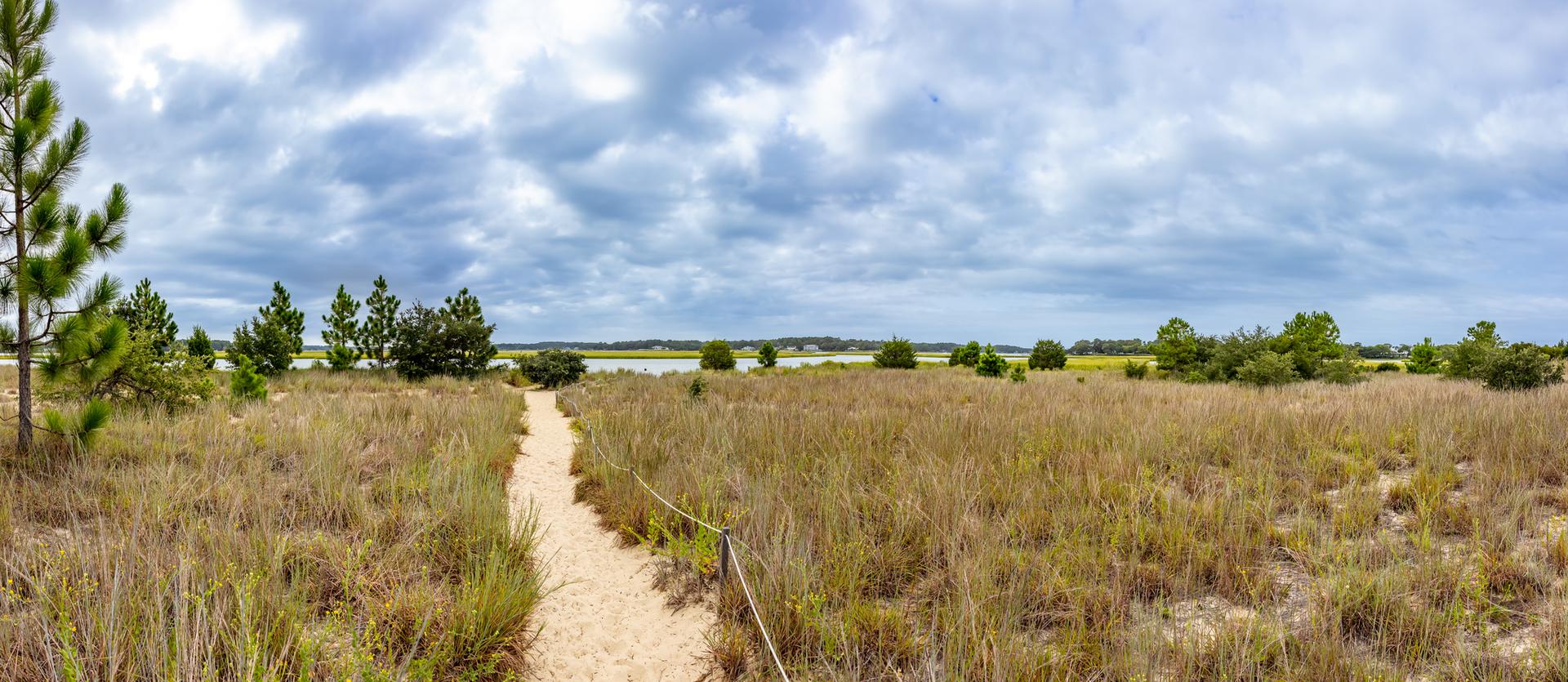 Sandy path winding through dry grassy fields under a cloudy sky.
