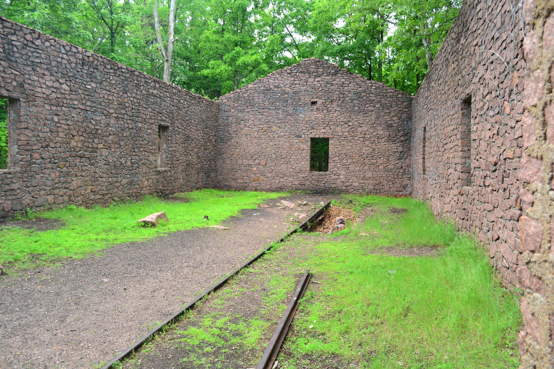 Ruined stone building walls with grassy floor and surrounding green trees.