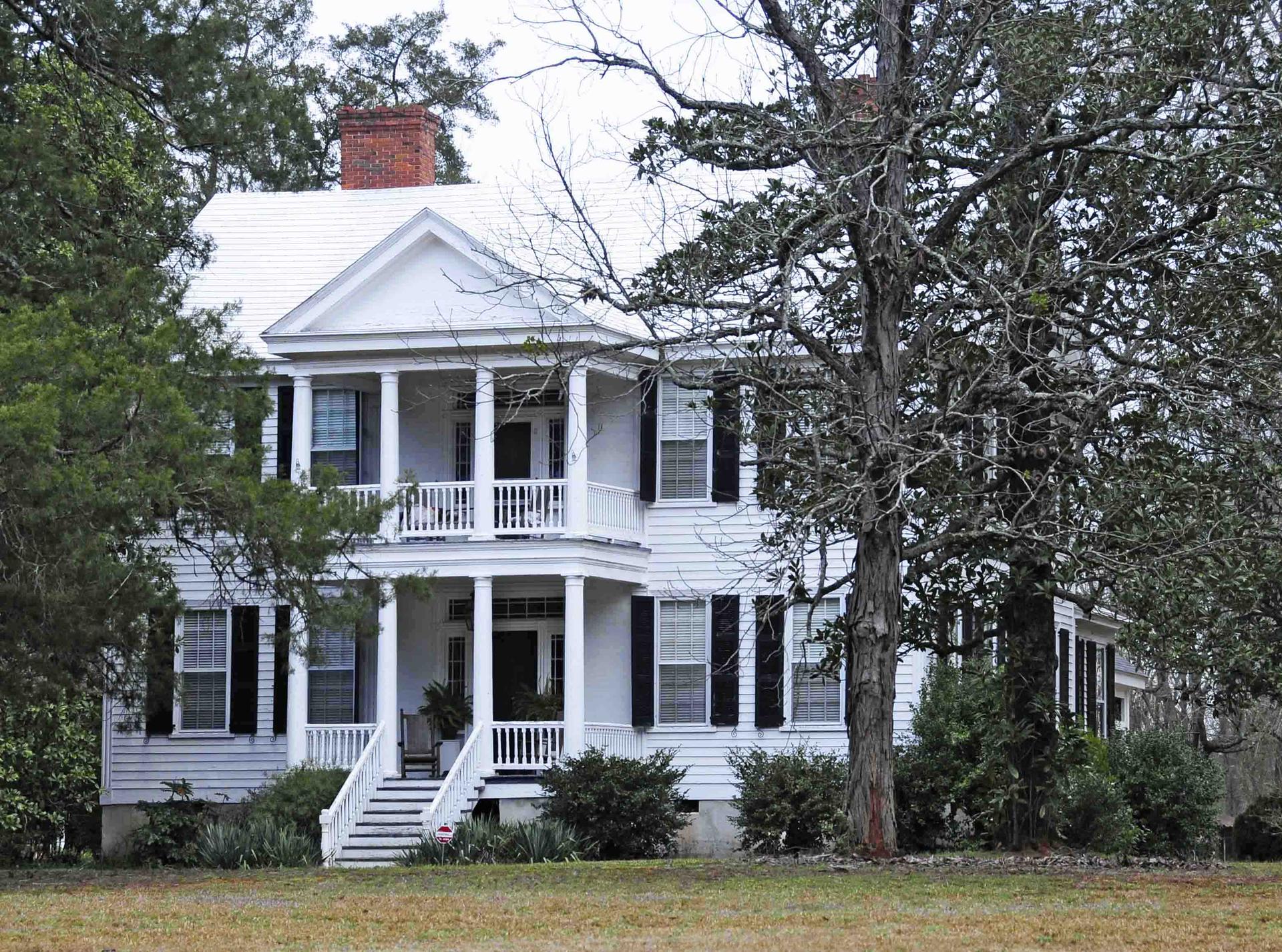 A large white house with columns and balconies, surrounded by trees.