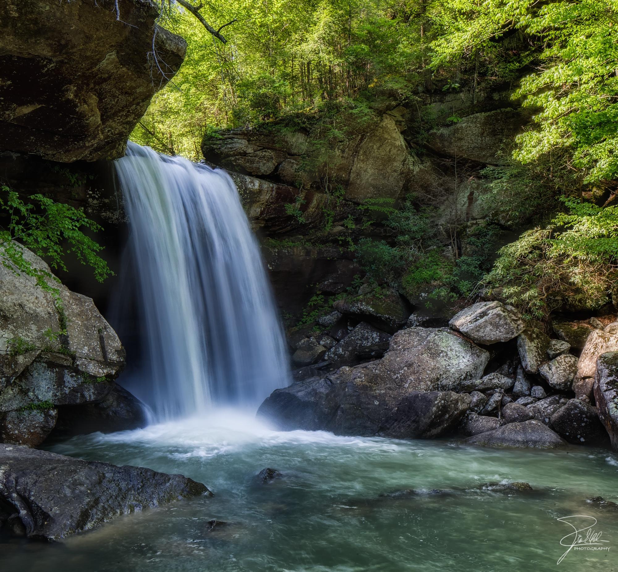 Powerful waterfall cascading into a rocky pool within a lush green forest.