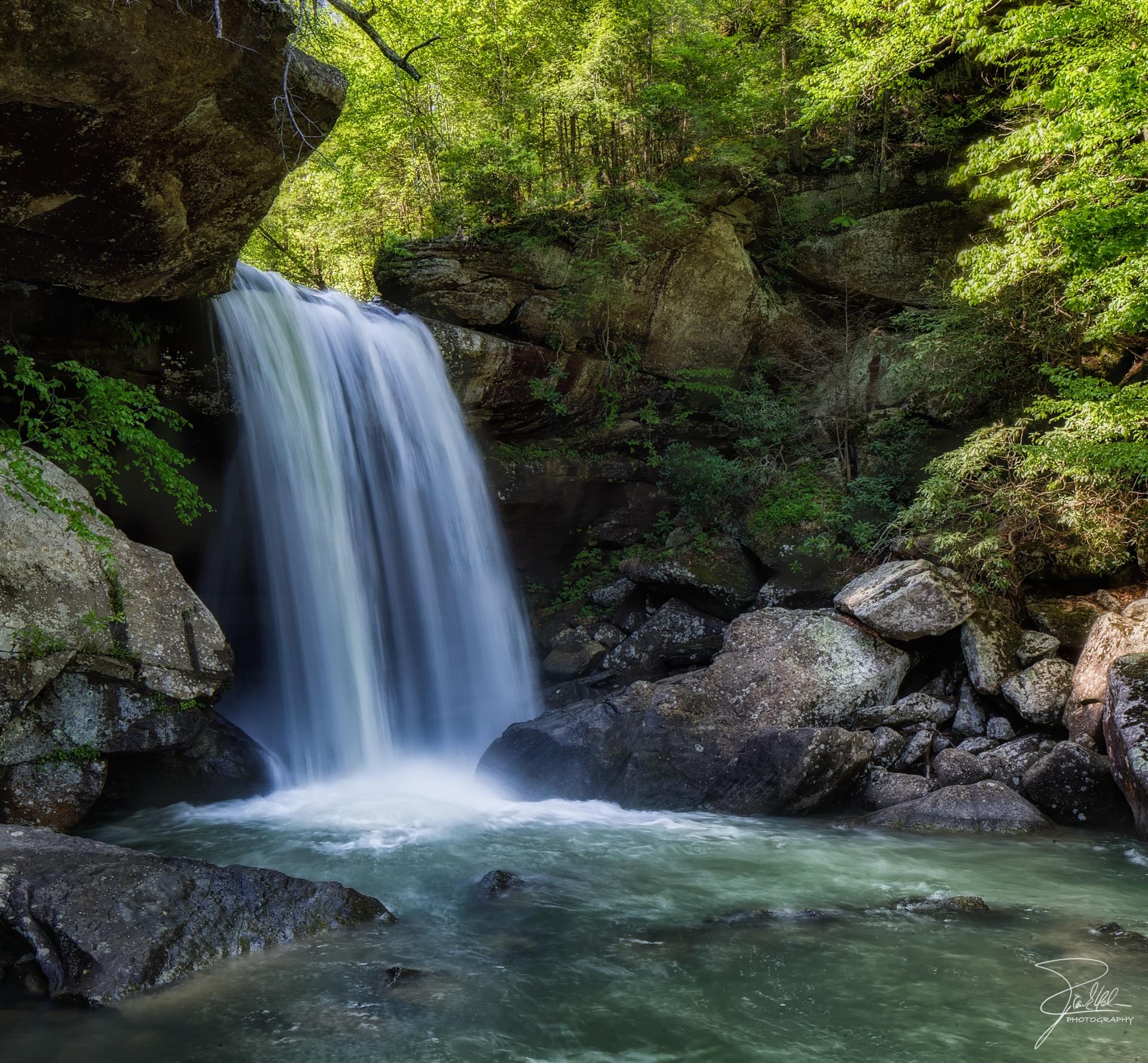 Powerful waterfall cascading into a rocky pool within a lush green forest.