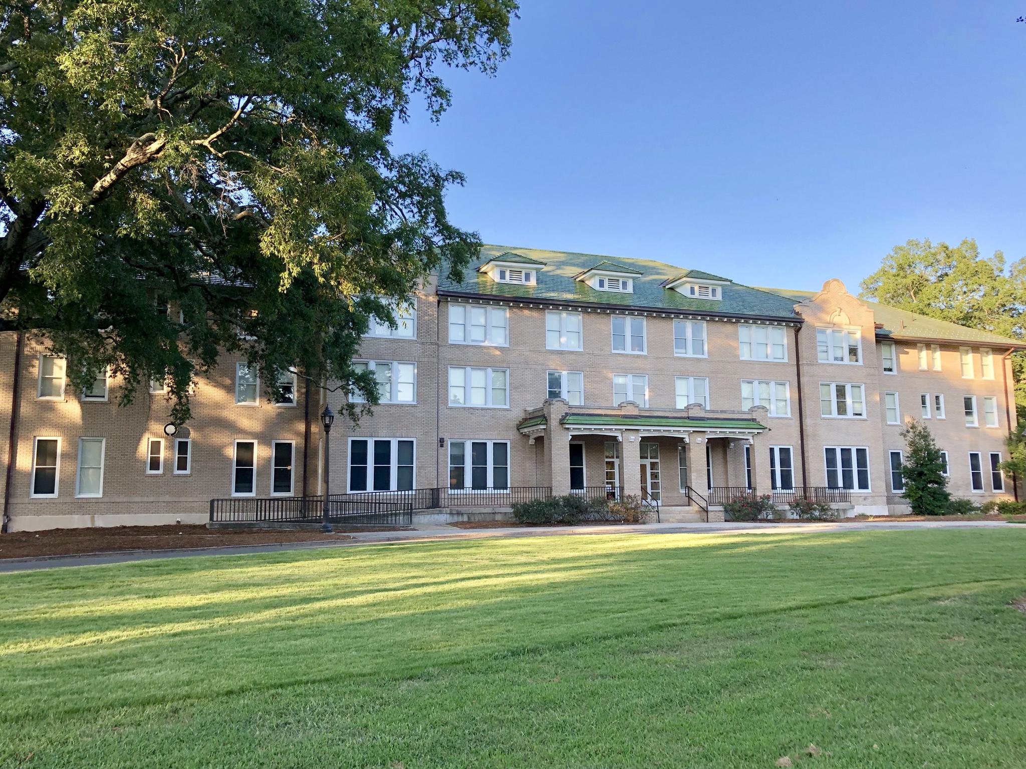 Multi-story building with green roof, large lawn, and trees in daylight.