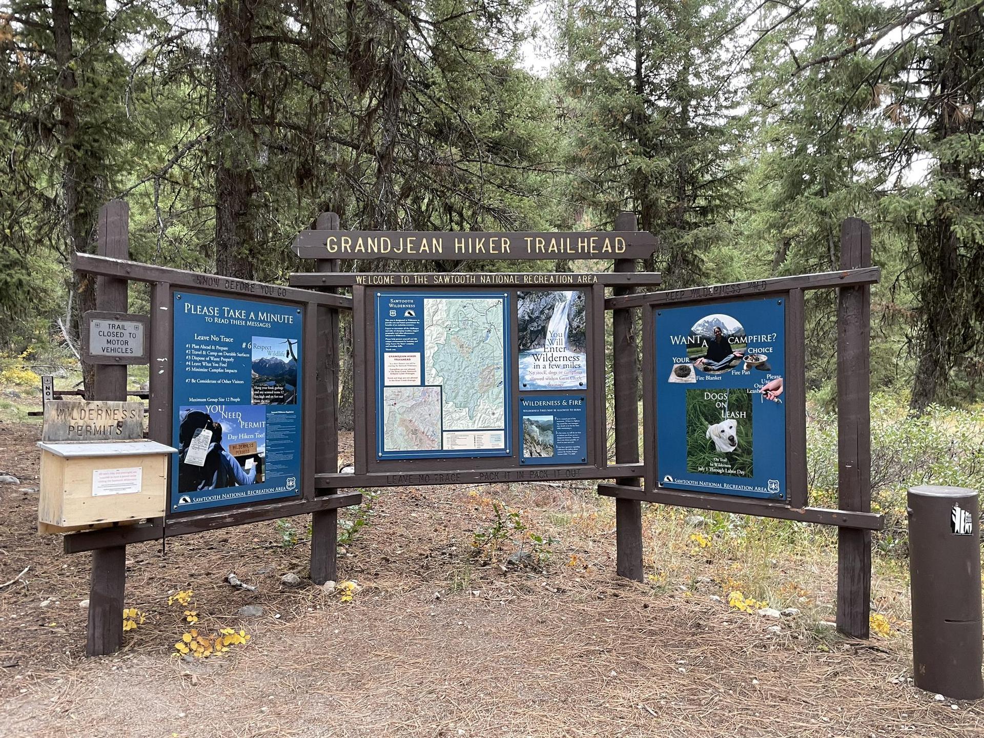 Wooden trailhead sign with information panels in a forest clearing.