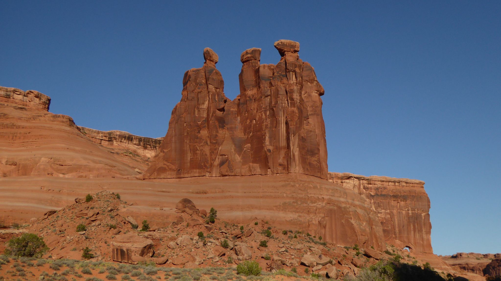 Three large red rock formations stand tall against a clear blue sky. - Park Avenue Trail