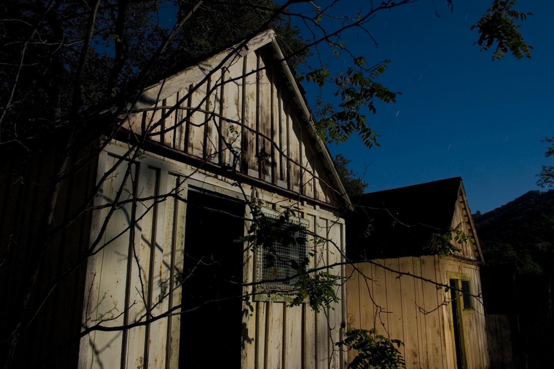 Two old wooden sheds illuminated at night under a dark blue sky.