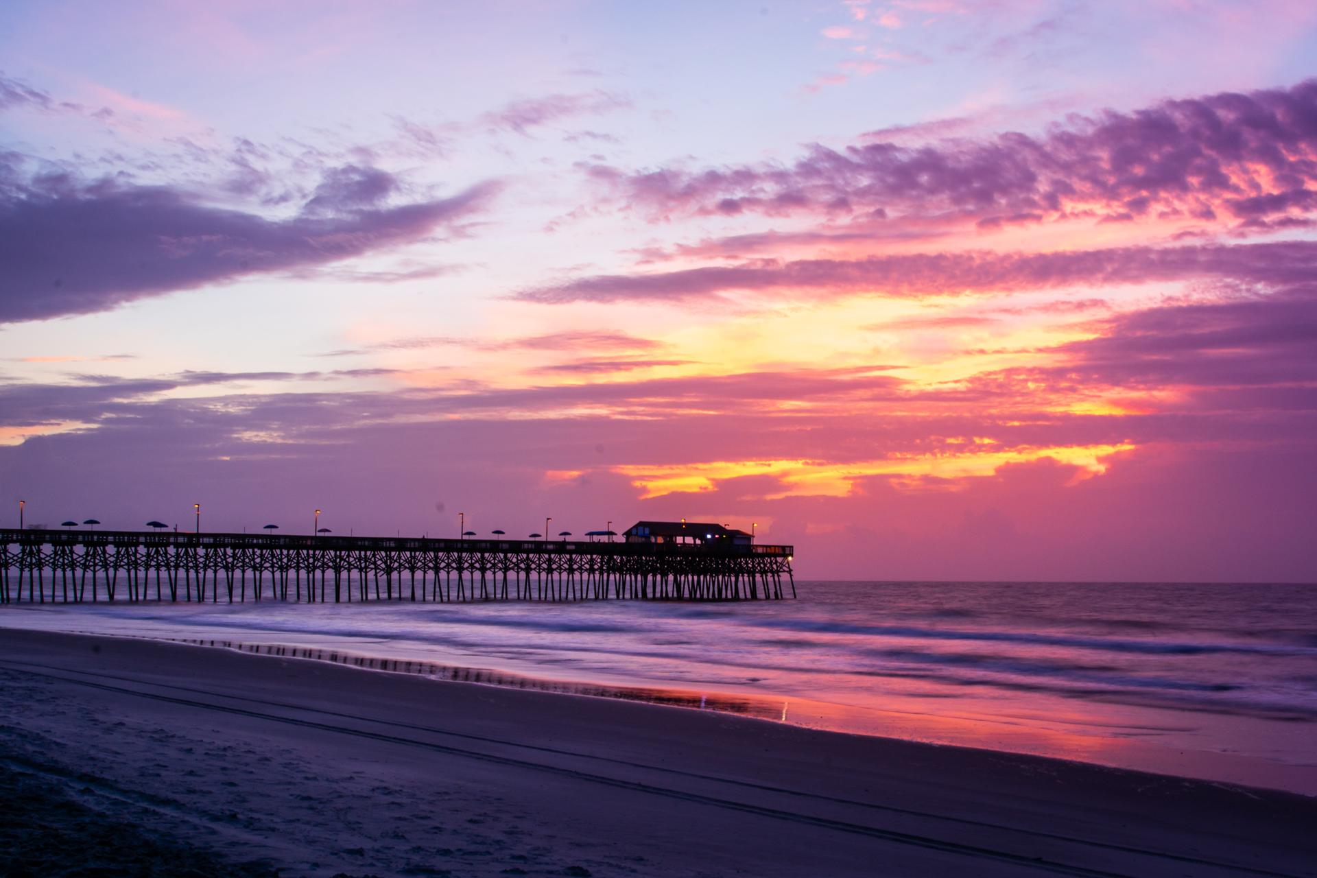 Colorful twilight sky above a long pier extending into the calm ocean.