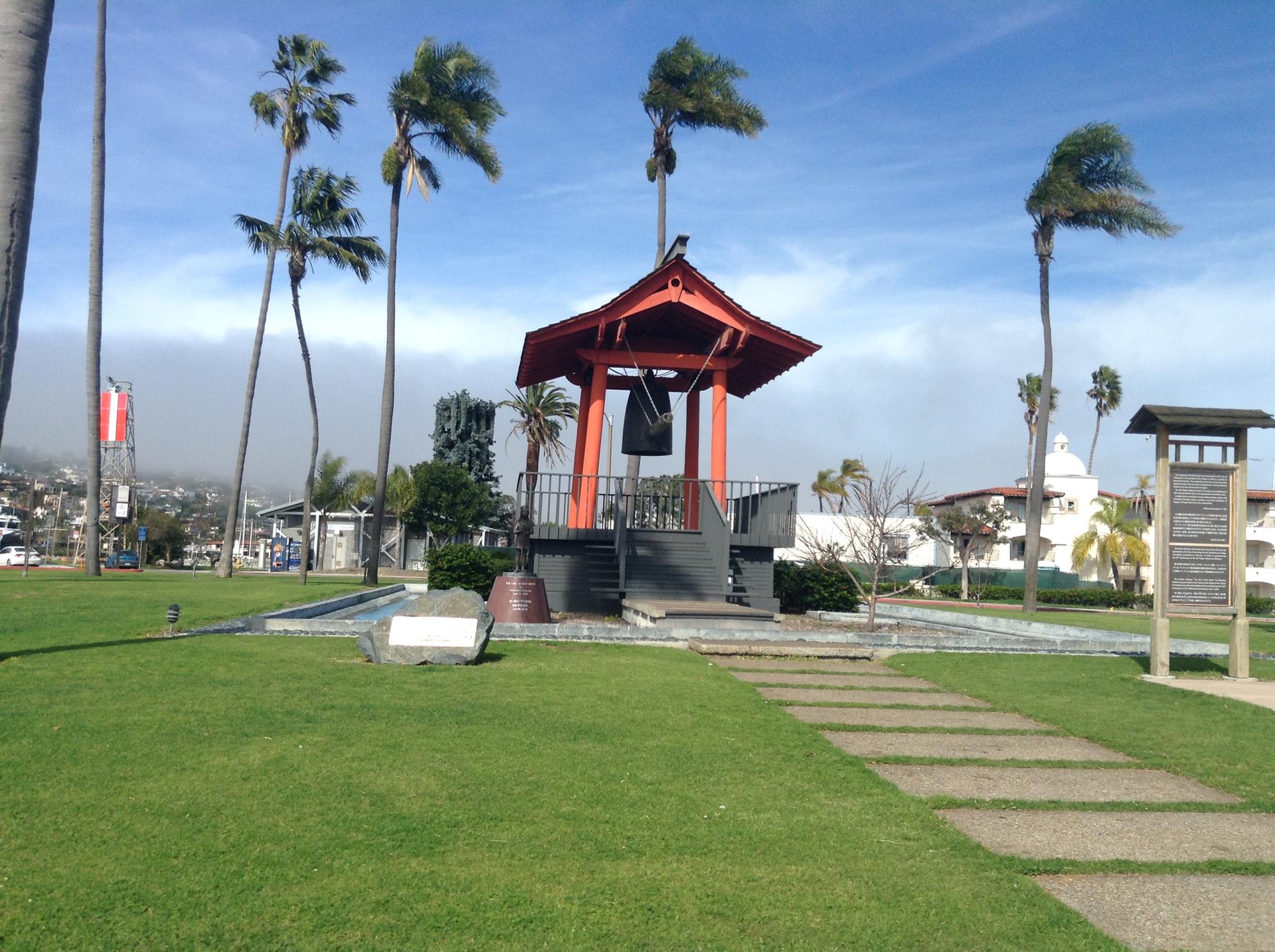Red pagoda-style structure with a bell in a sunny park with palm trees.