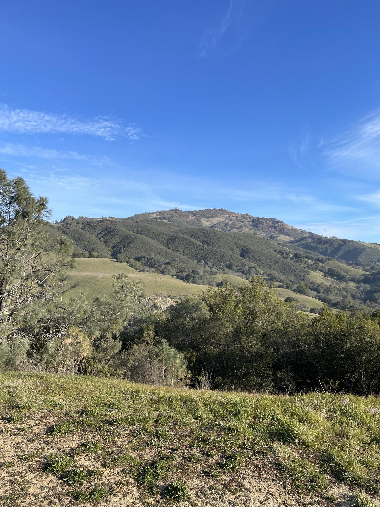 Expansive view of green hills and mountains under a bright blue sky.