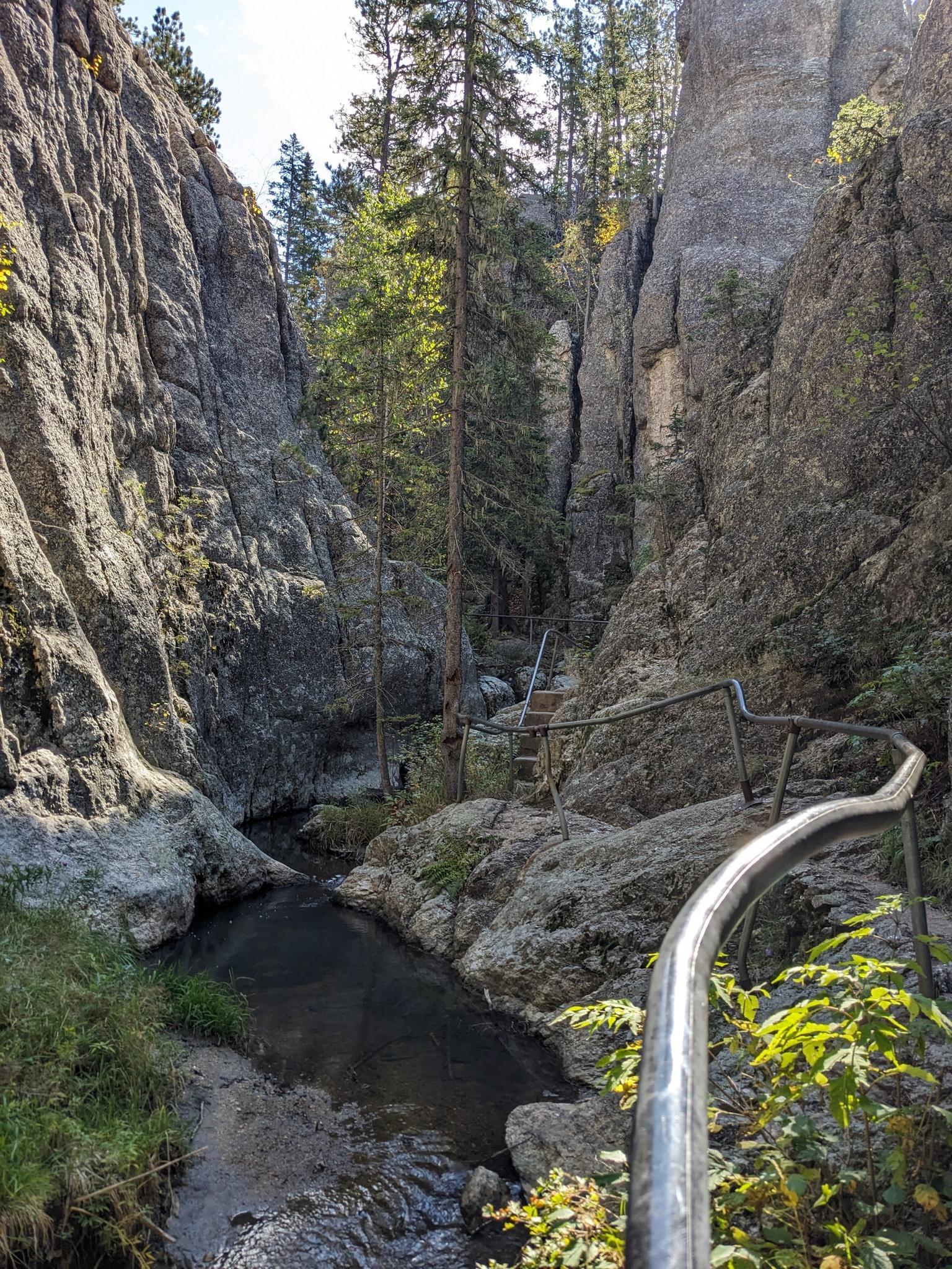 Stream flowing through a narrow rocky canyon with a metal handrail.