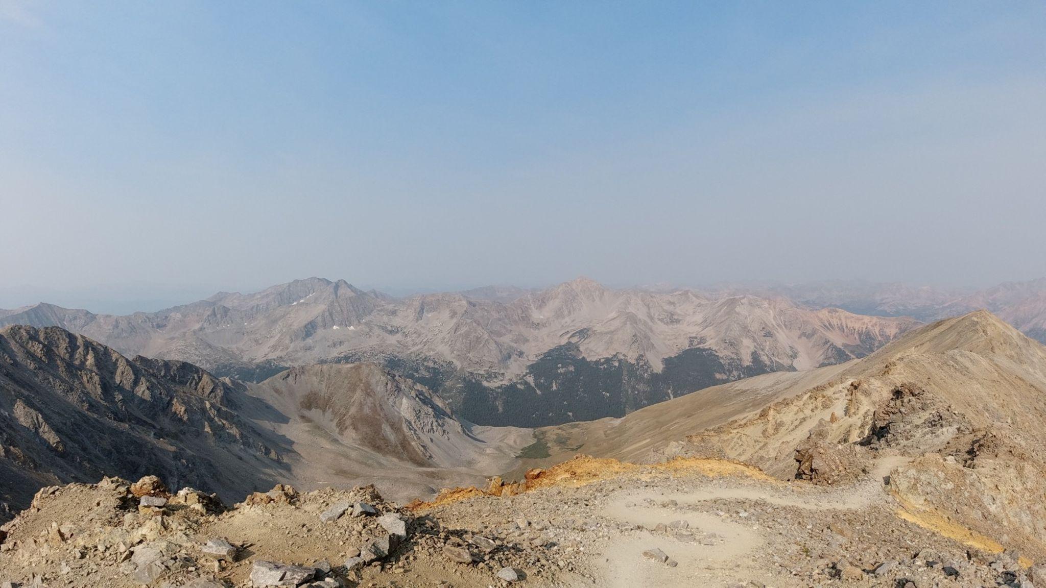 Vast, hazy mountain range with rocky peaks under a bright sky.