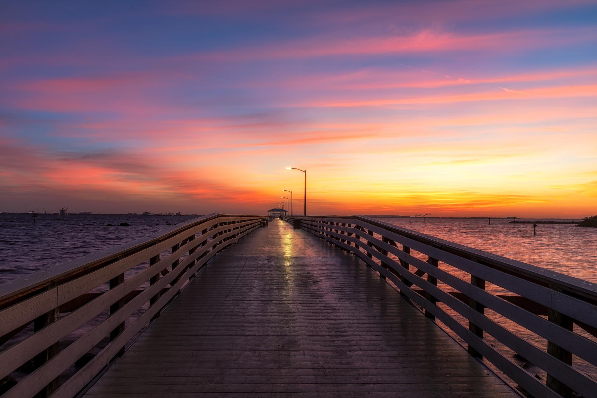 Long wooden pier extending over water under a vibrant sunset sky.