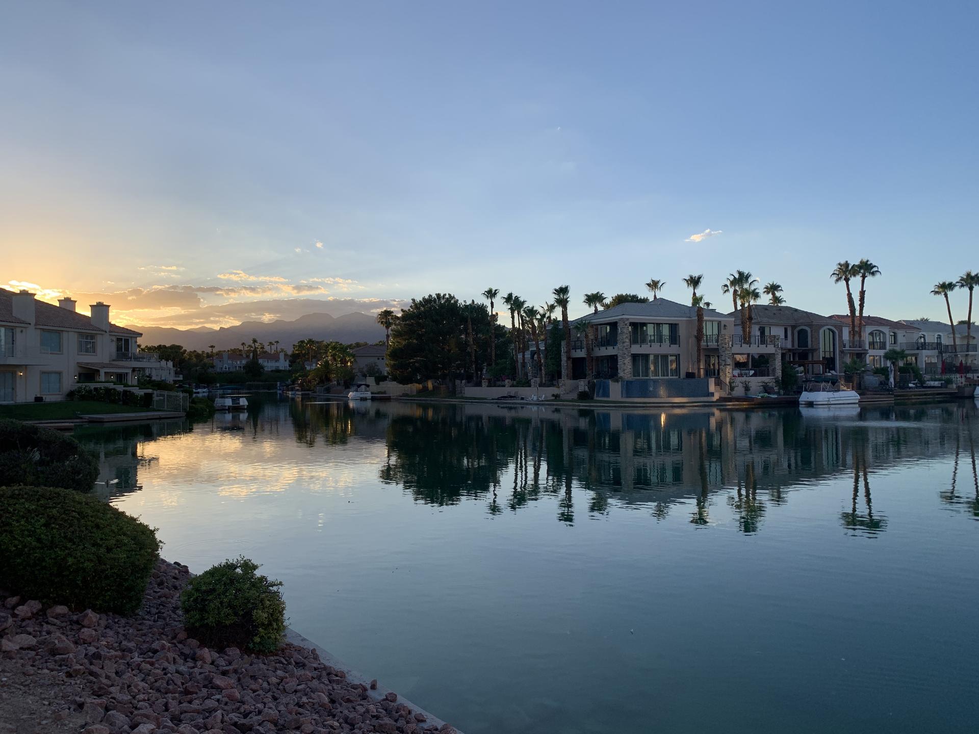 Waterfront houses reflecting in a calm lake at sunset.