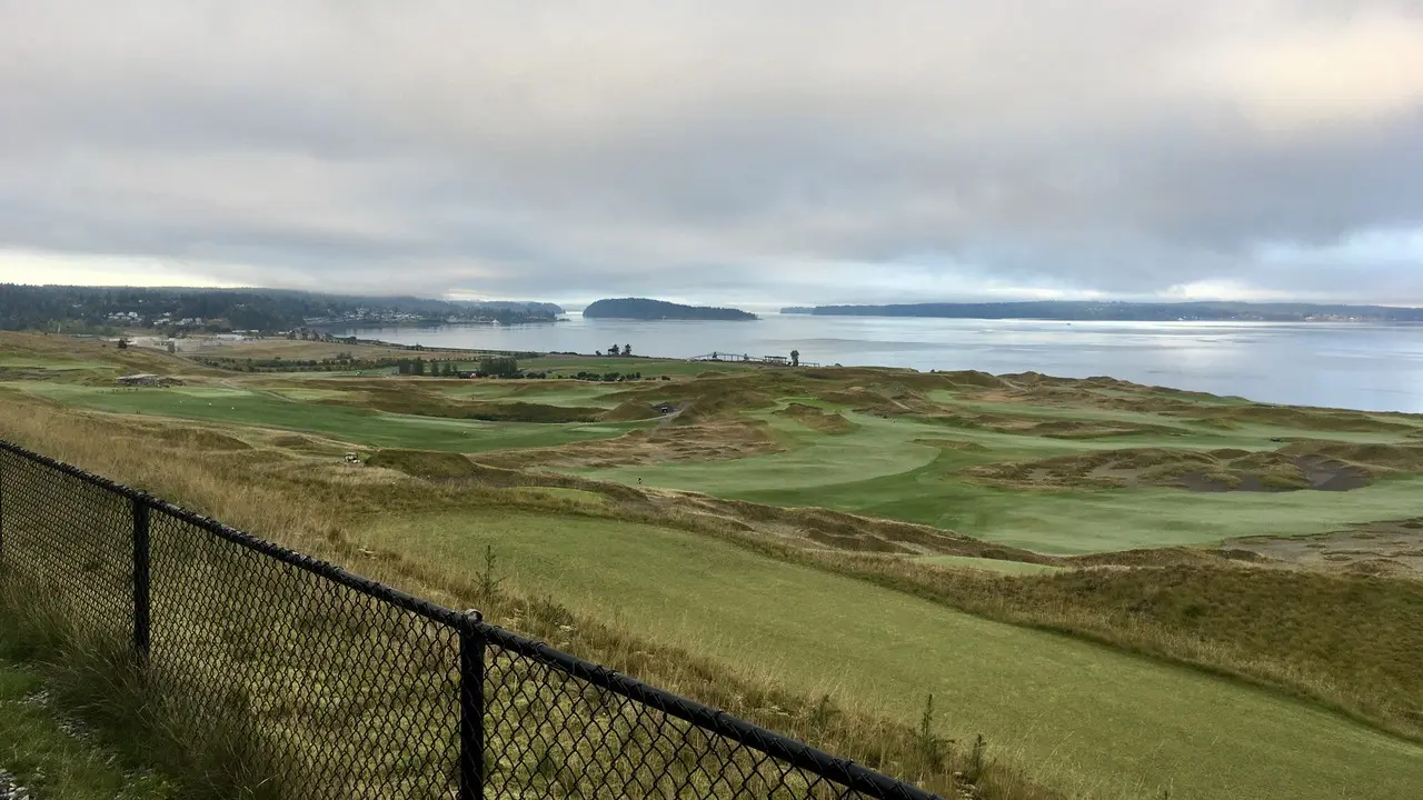 Overcast view of a coastal golf course with a fence and distant town.