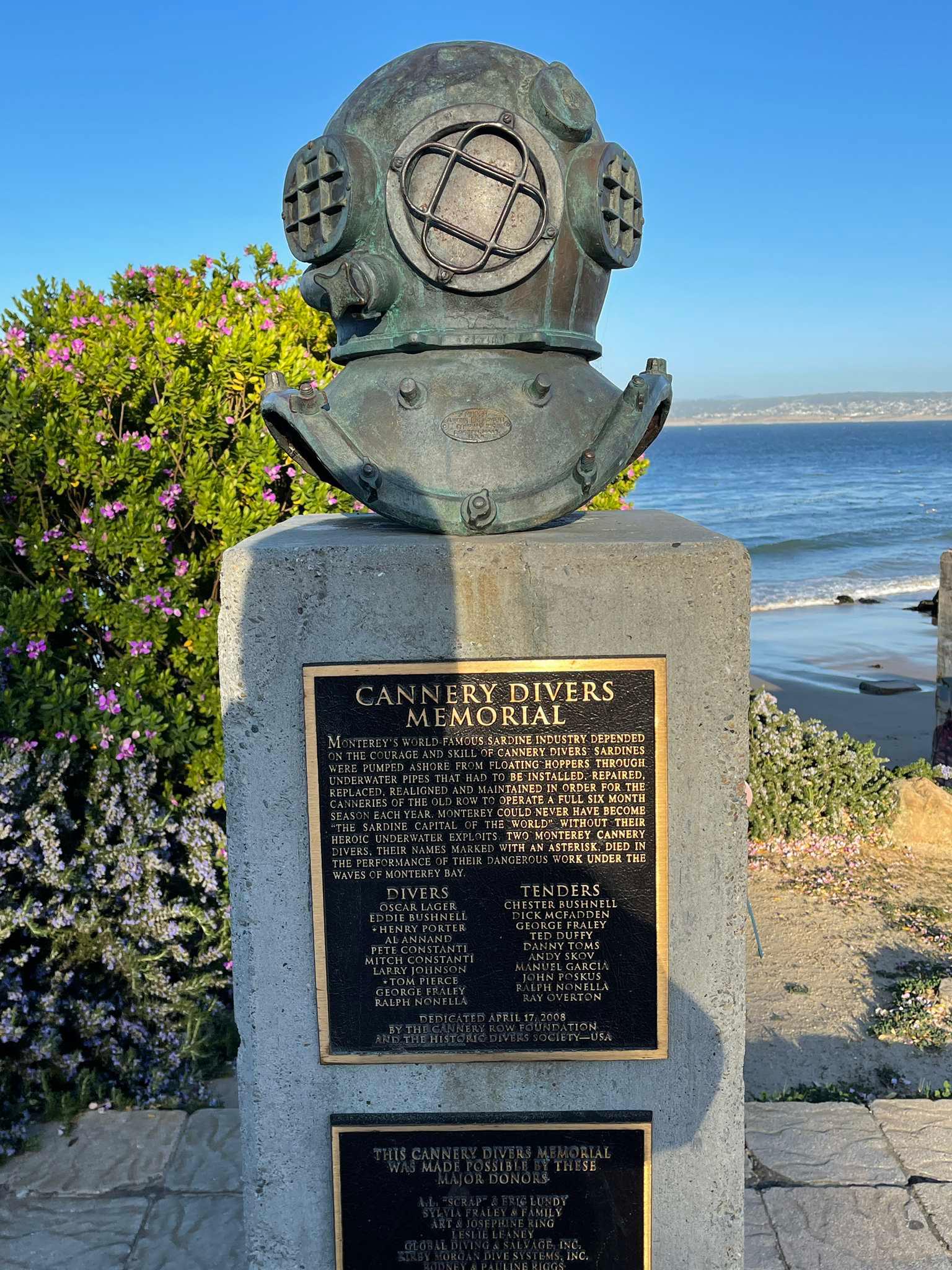 Bronze diver's helmet memorial on a pedestal overlooking the ocean.