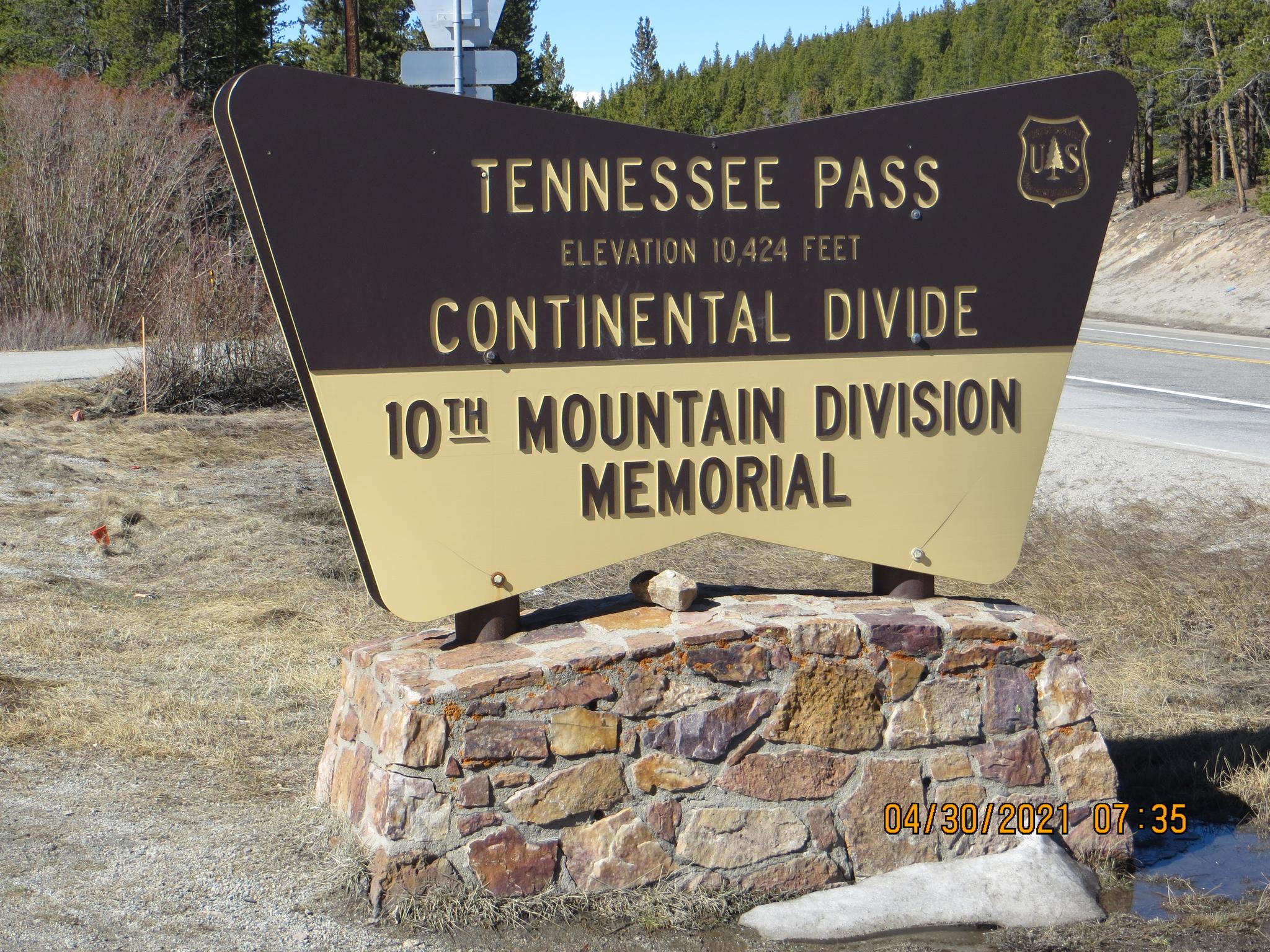 A large brown and gold sign on a stone base next to a road.