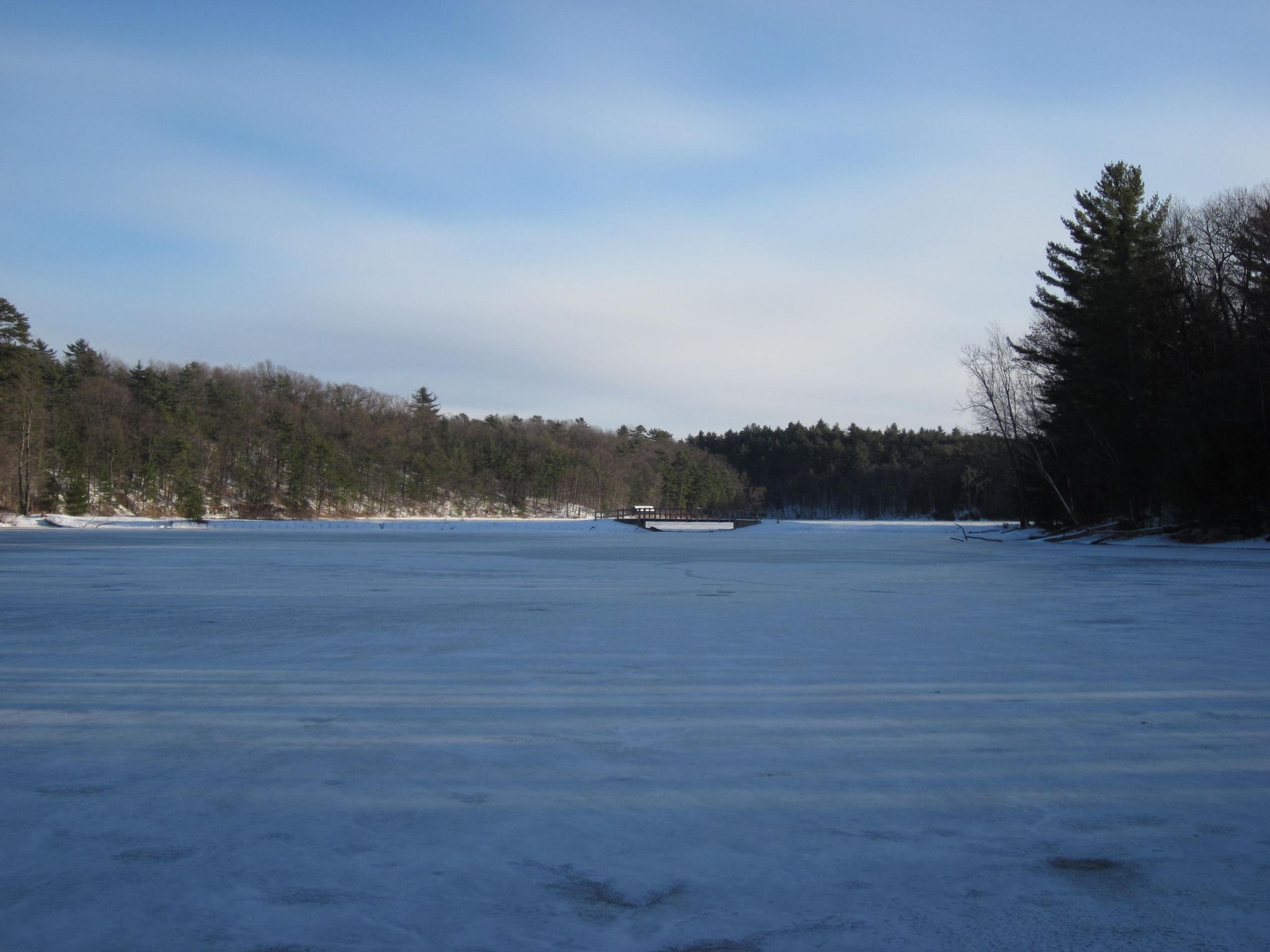 A frozen lake surrounded by snow-dusted evergreen and bare trees under a clear sky. - Frozen Moreau Lake loop from Town of Moreau