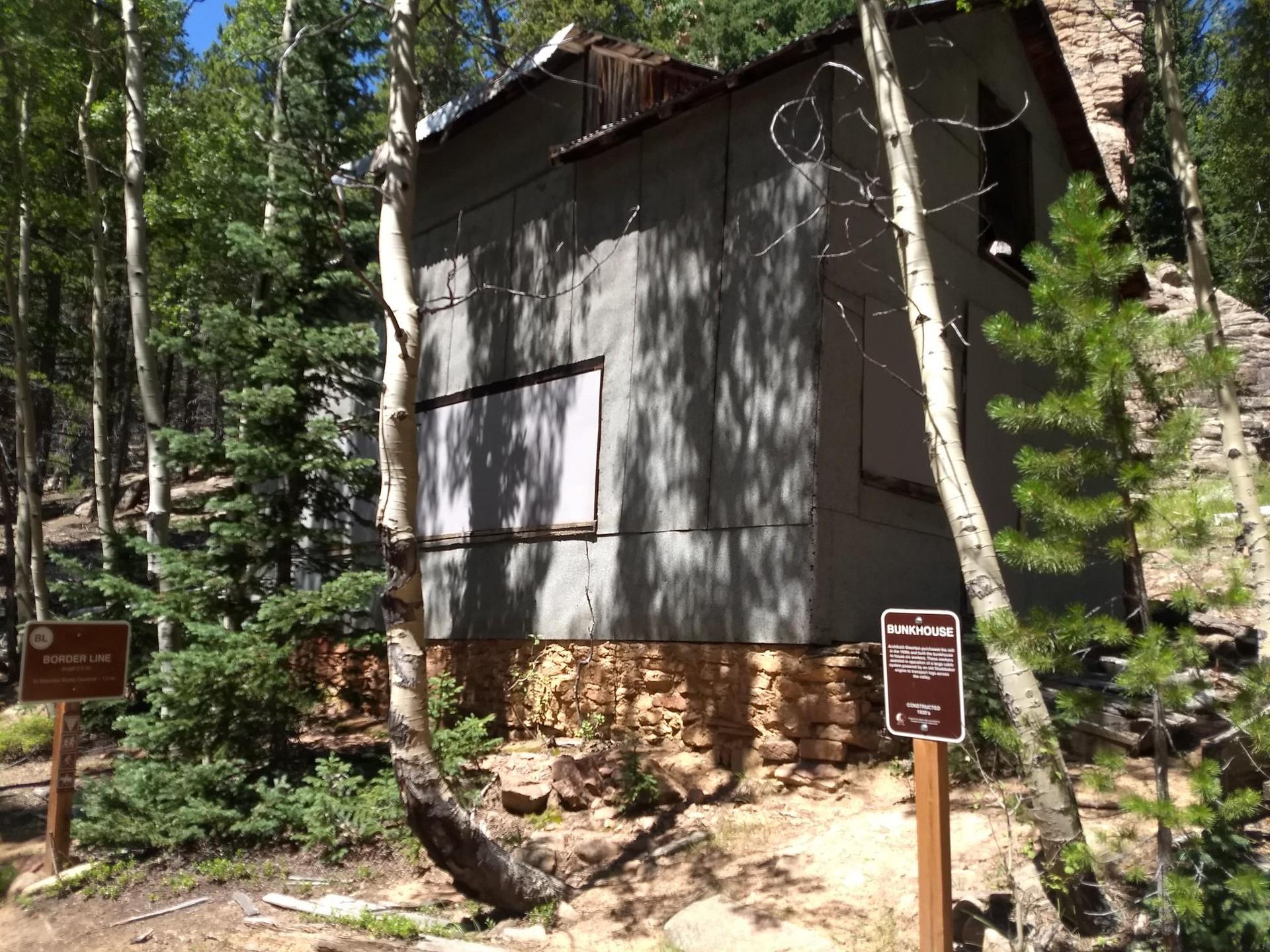 An old, weathered building with boarded windows, surrounded by trees and signs.