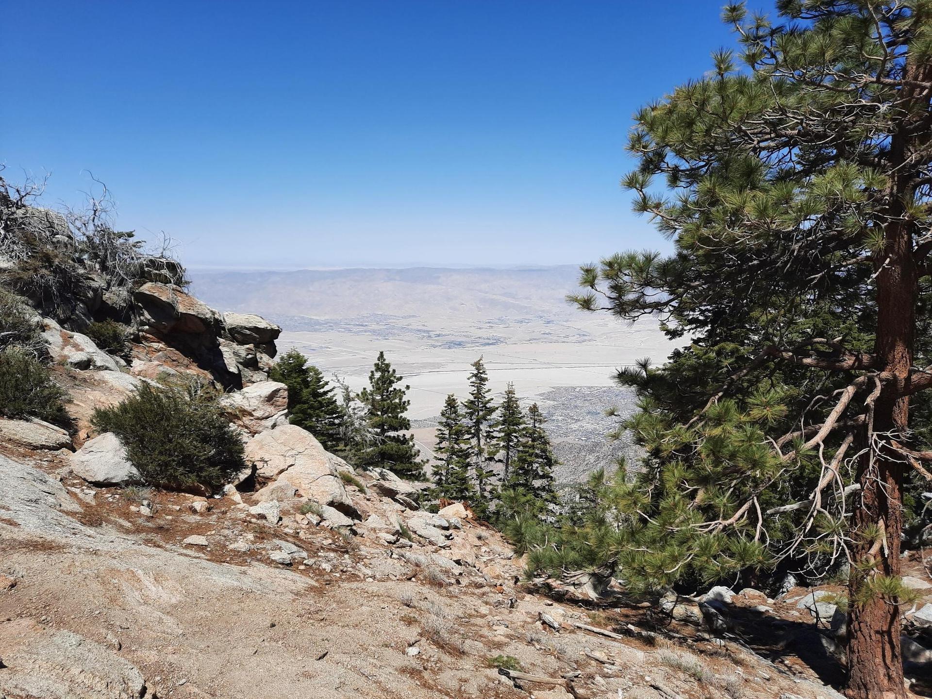 Rocky mountain slope overlooking a vast arid valley under a clear blue sky.