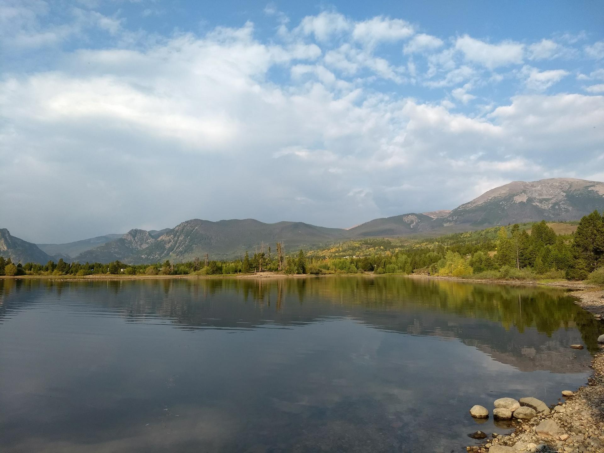Calm lake reflecting trees and sky, with forested shores and mountains.