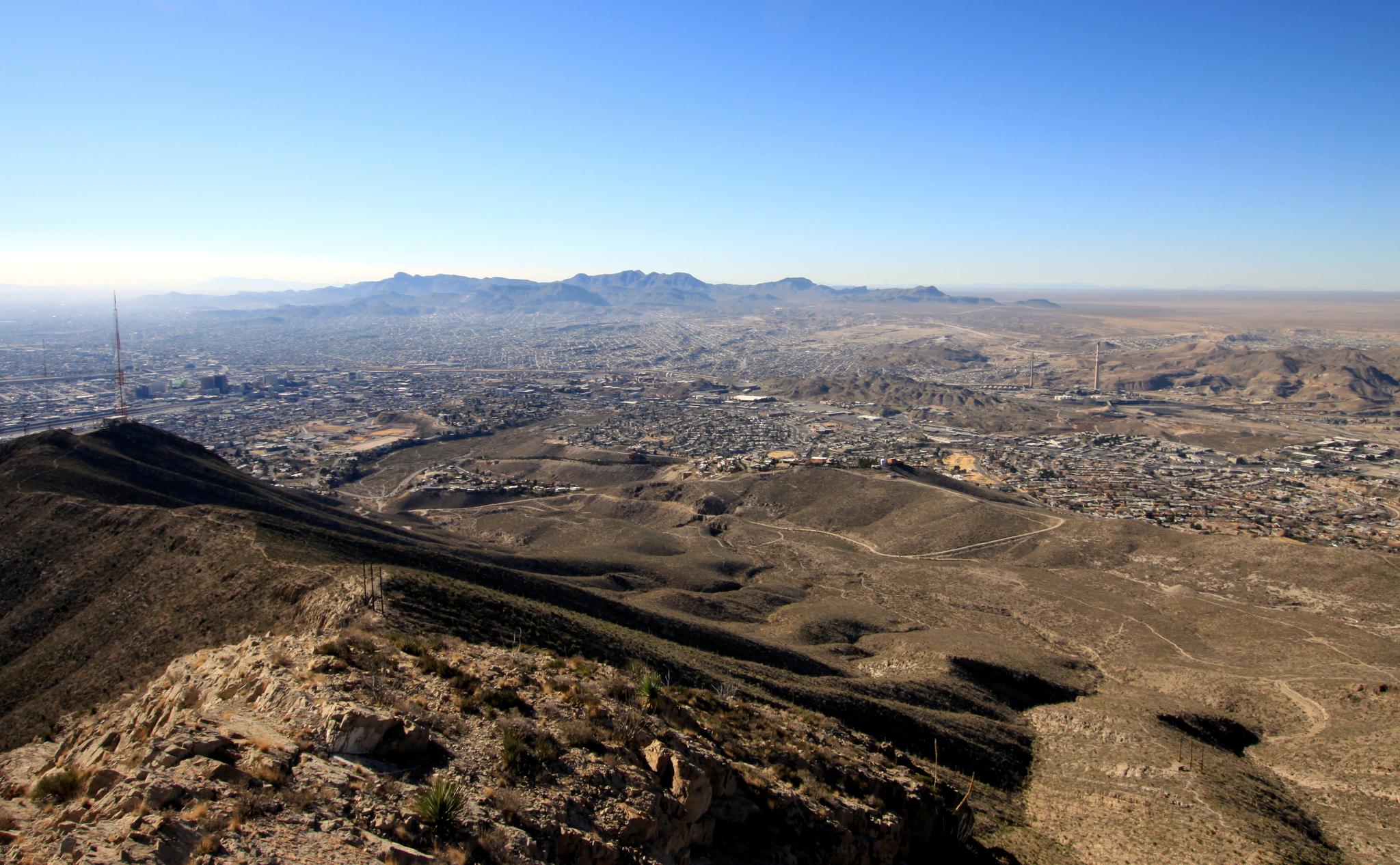 Expansive aerial view of a city nestled among desert mountains under clear skies.