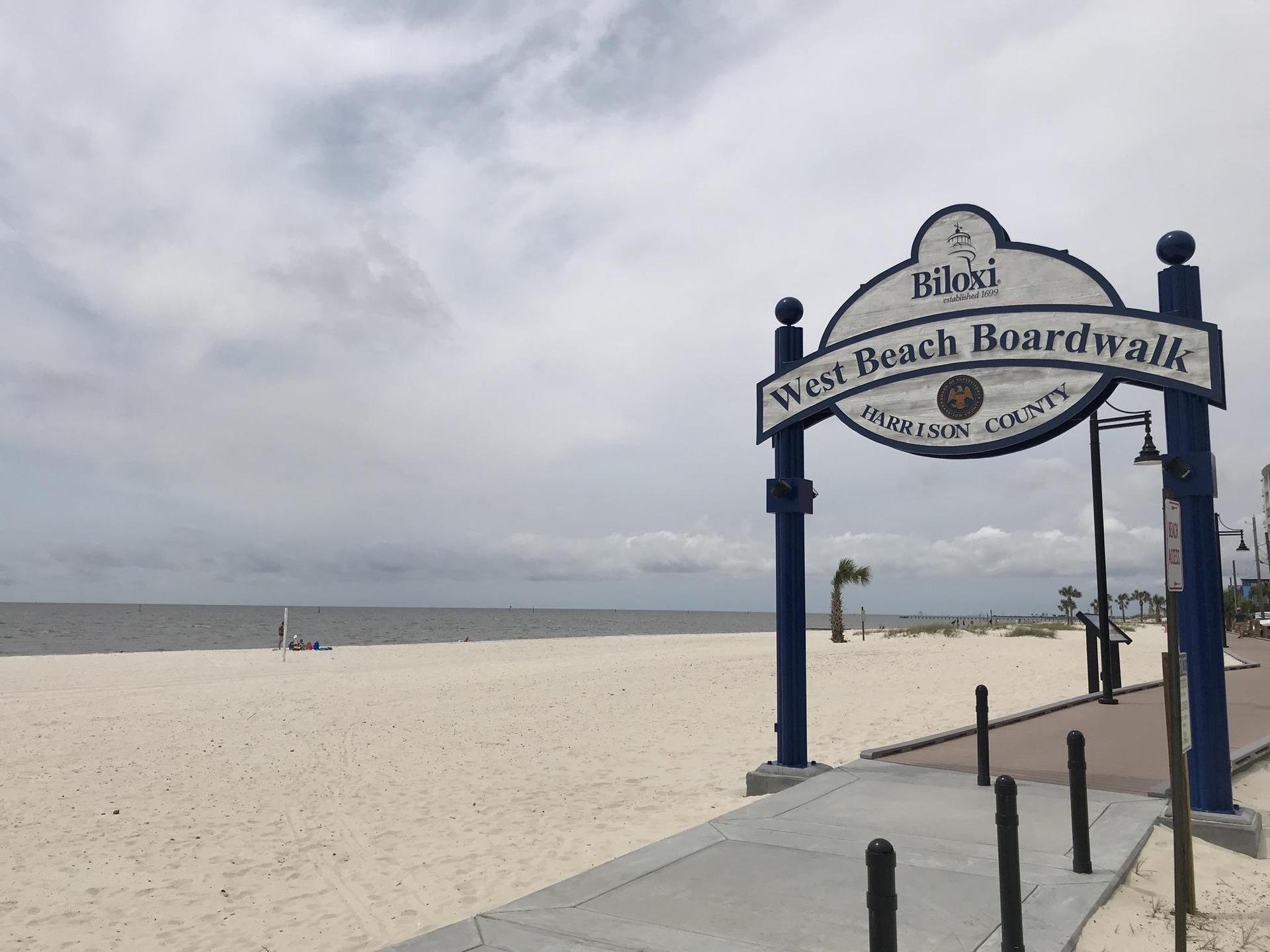 A sign for a boardwalk on a wide sandy beach under a cloudy sky.