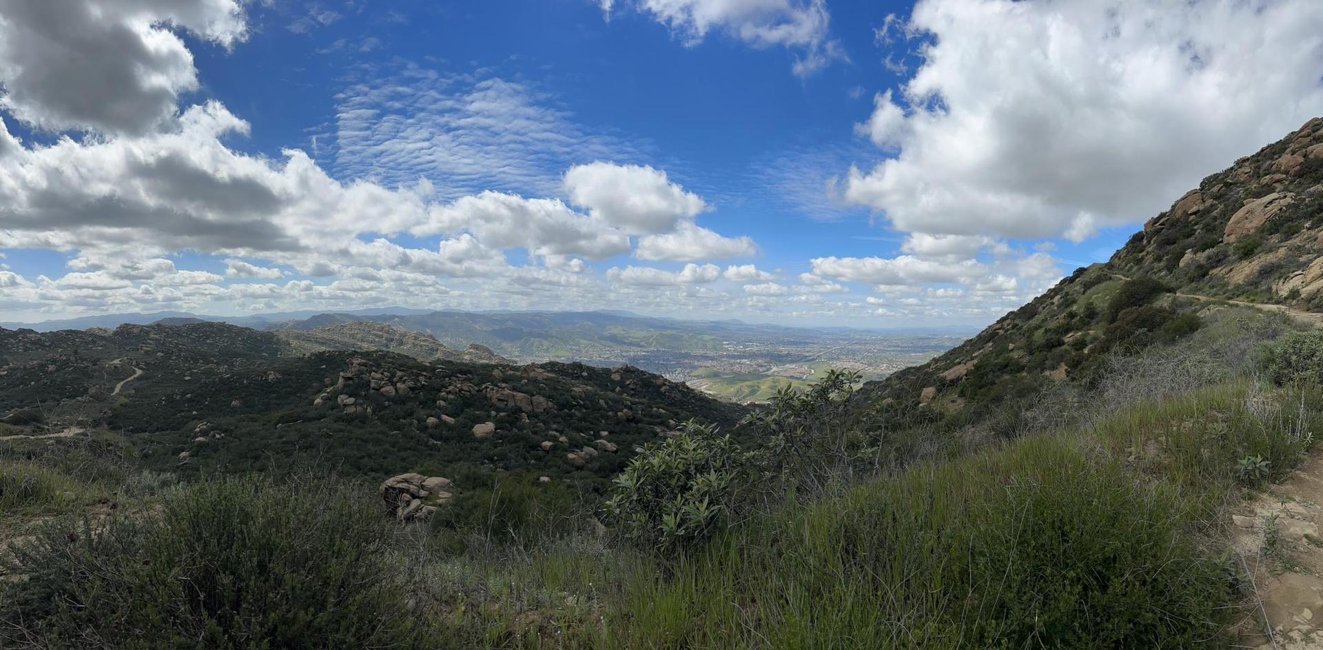 Panoramic view of rocky, green hills under a bright, cloudy sky.