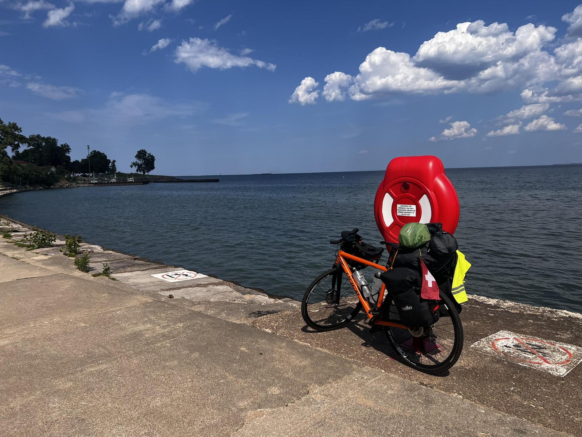 Touring bicycle with gear parked by a large body of water under a sunny sky.
