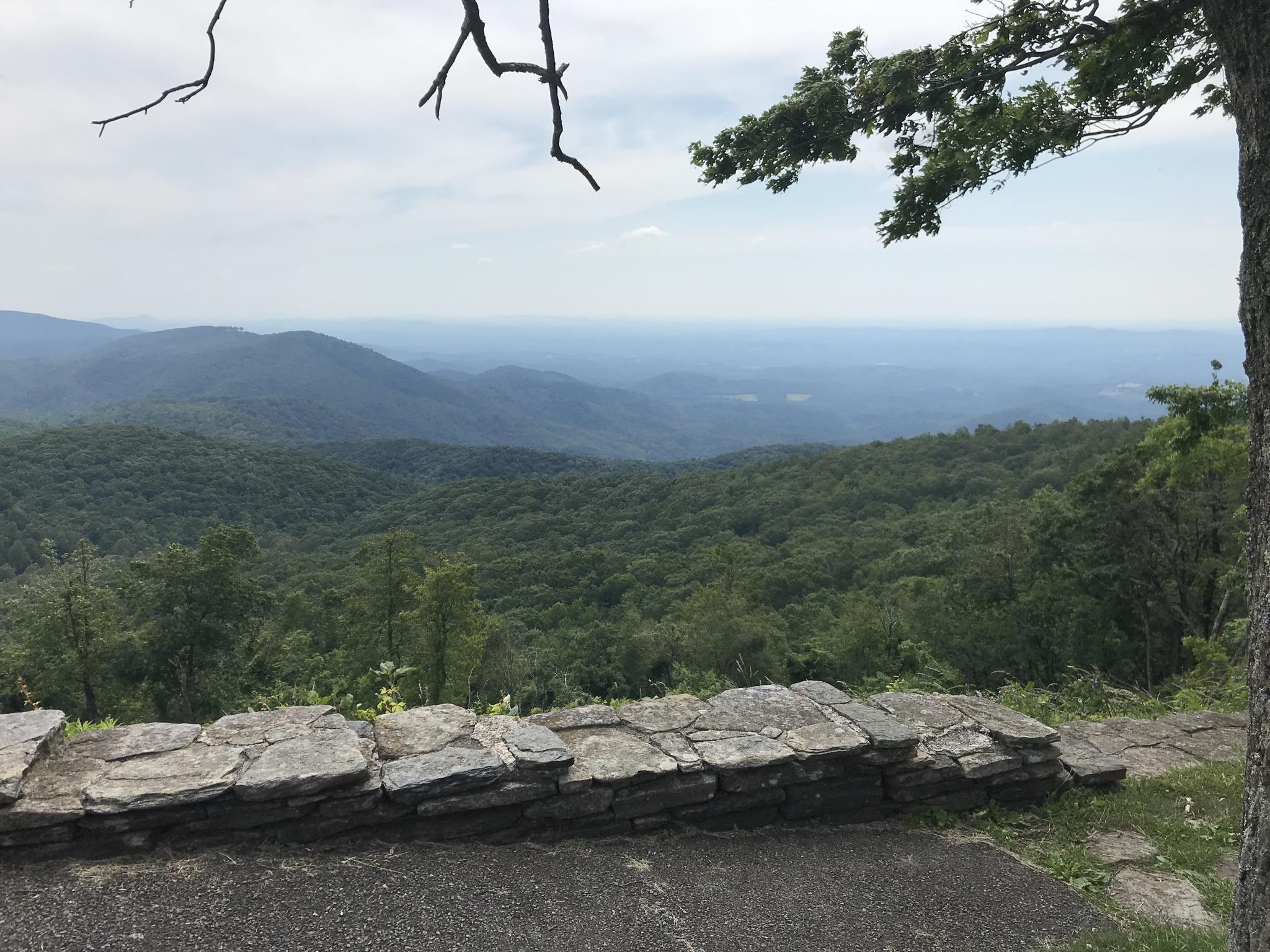 A stone wall overlooks layered green mountains under a cloudy, hazy sky.