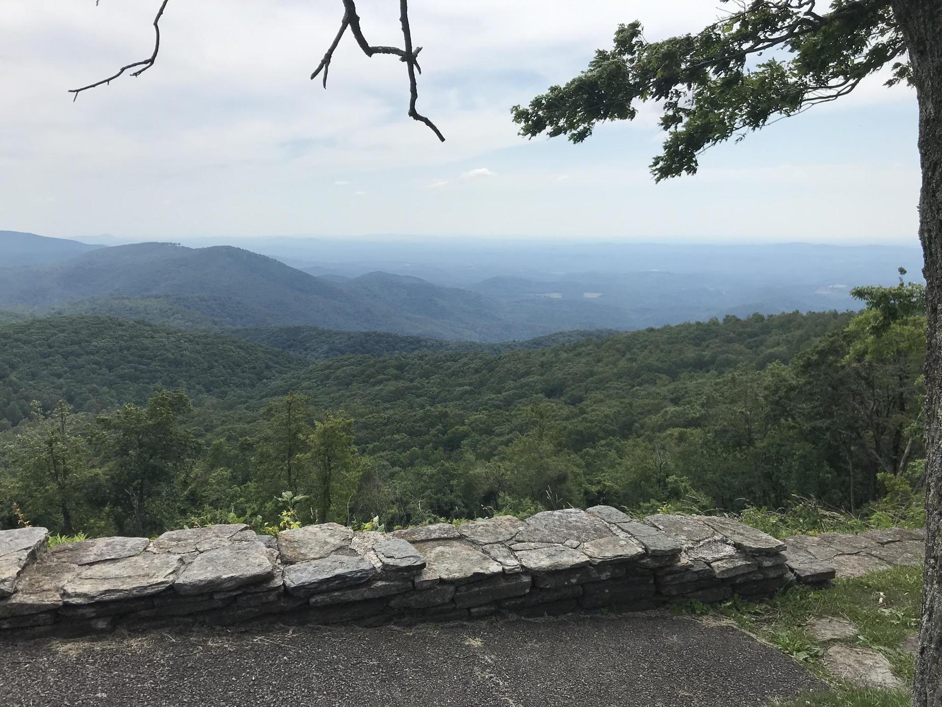 A stone wall overlooks layered green mountains under a cloudy, hazy sky.