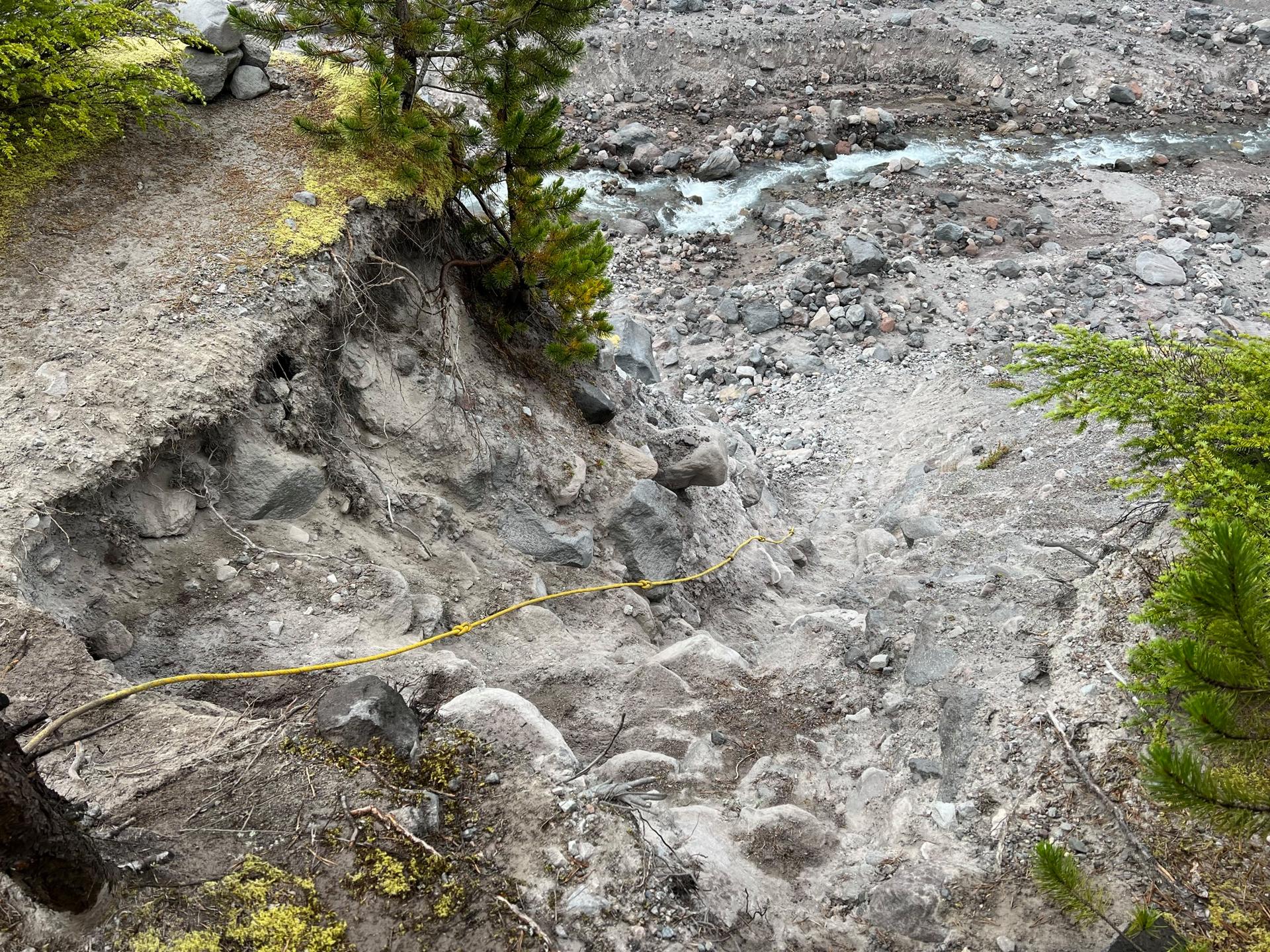 An eroded dirt trail overlooking a rocky riverbed with light blue water.