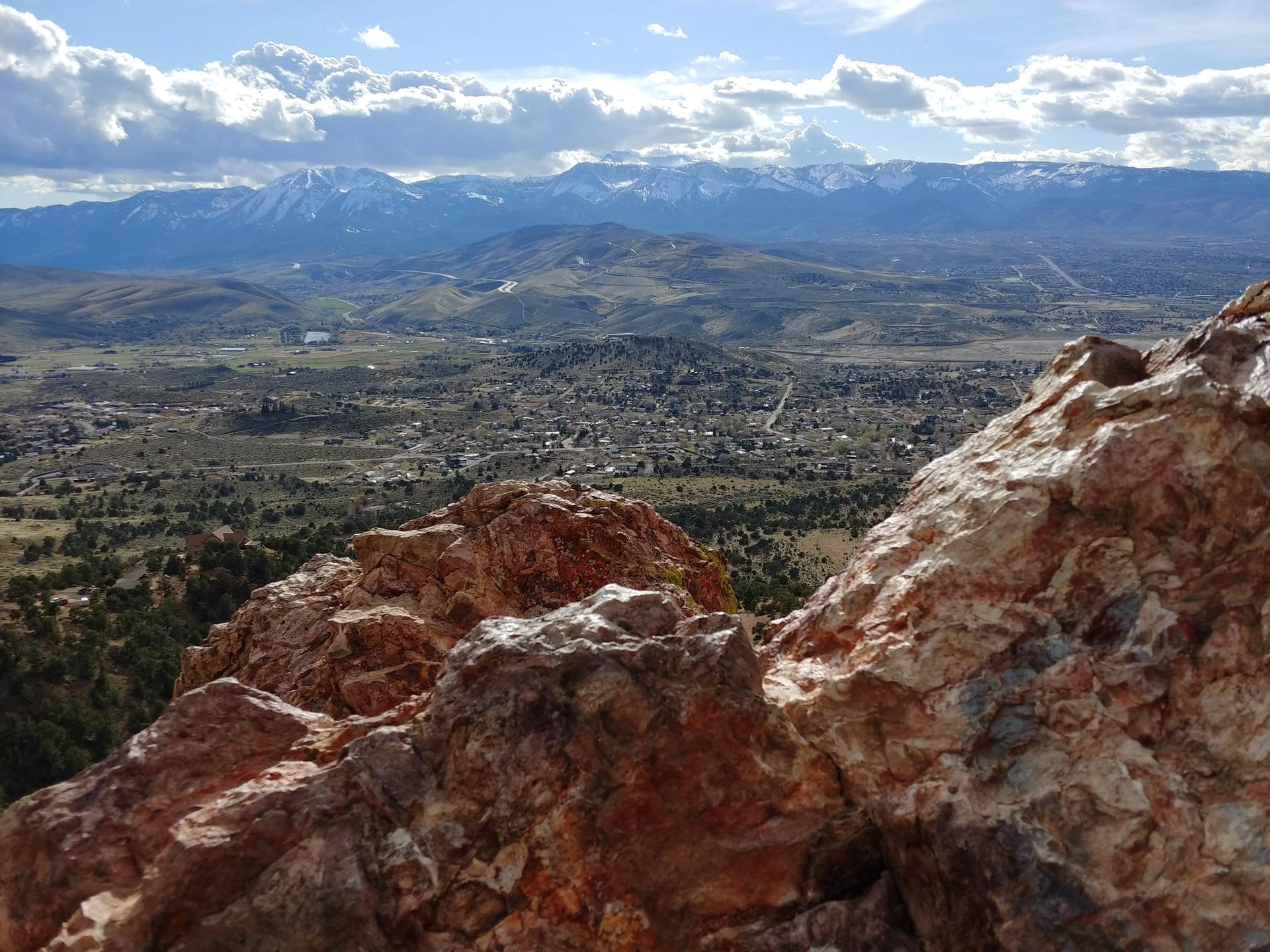 Rugged orange rocks overlook a valley town and distant snow-capped mountains.