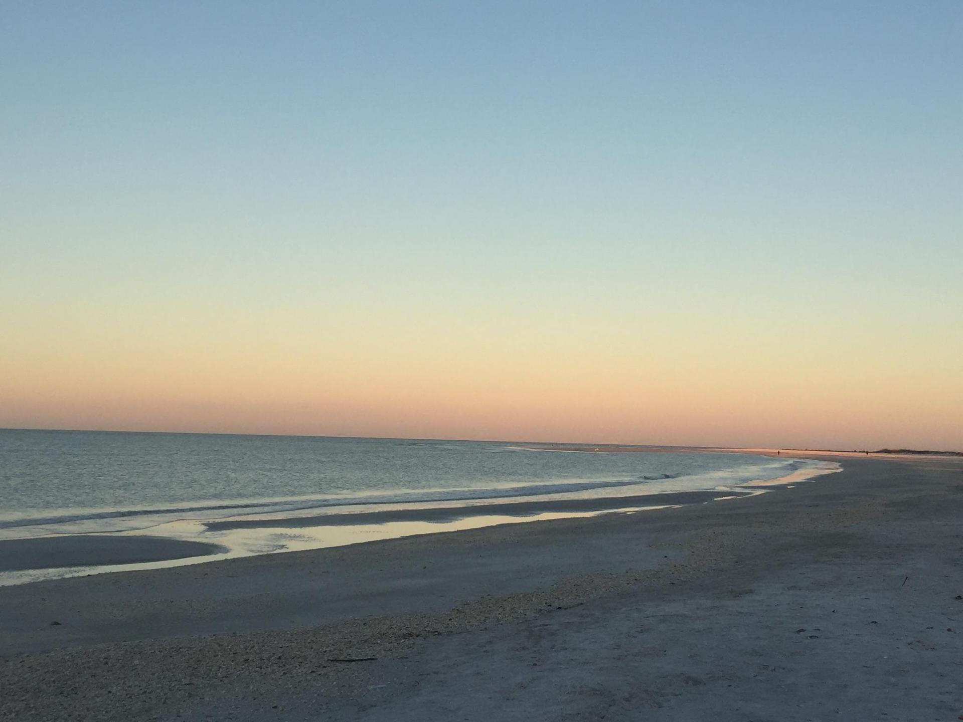 A tranquil sandy beach meets the ocean under a soft, colorful twilight sky.