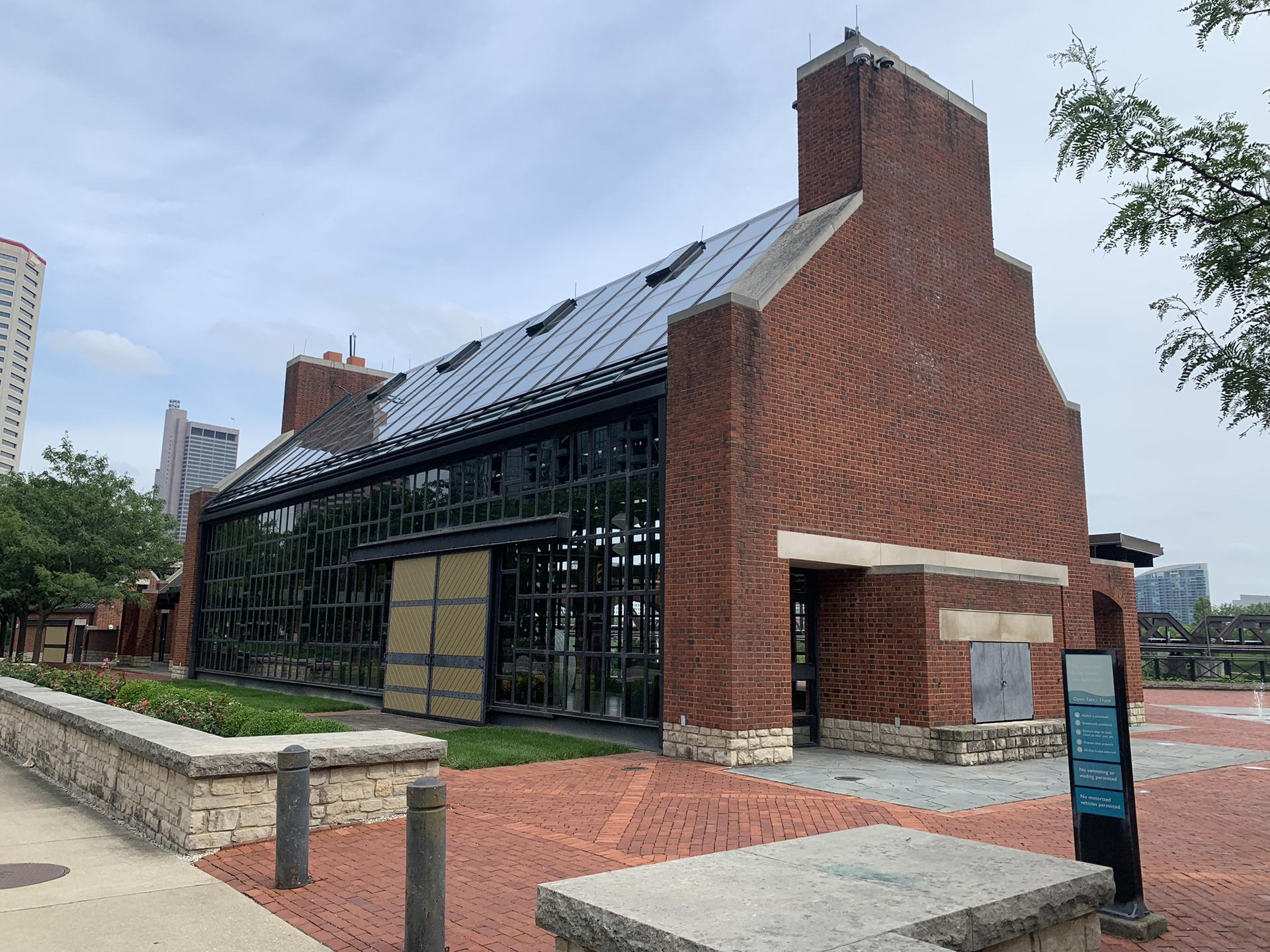 Large brick building with glass walls and a paved area under a cloudy sky.