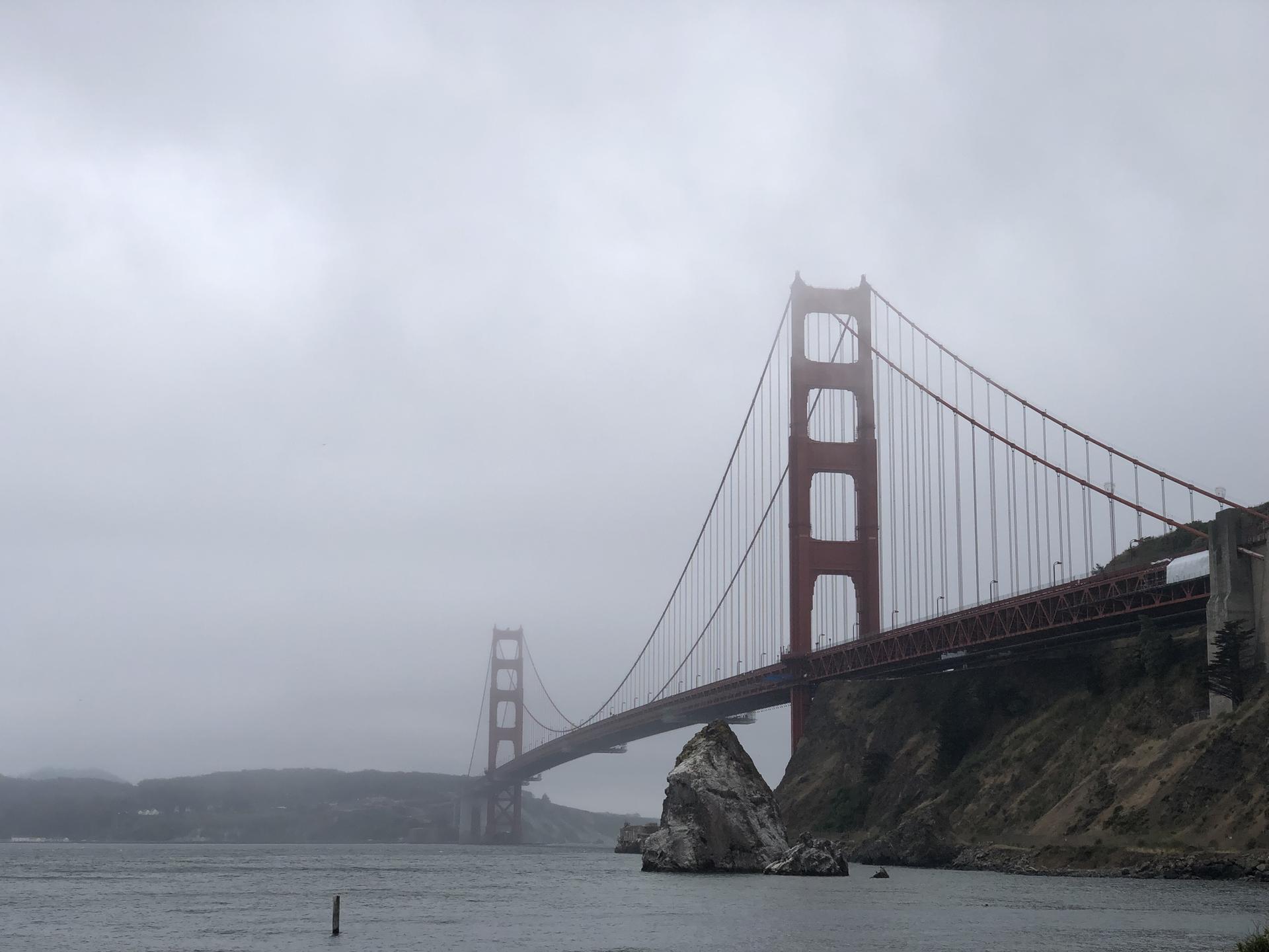 Red suspension bridge partially obscured by heavy fog over water.