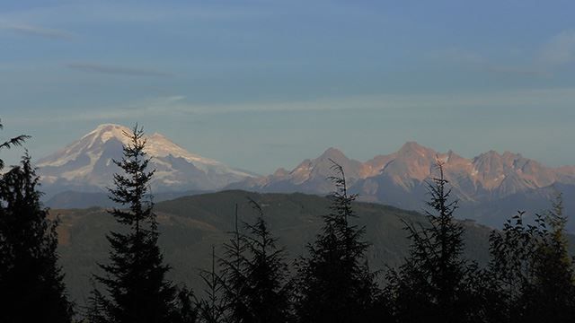 Distant snow-capped mountains and a rugged range under a clear sky, framed by trees. - Lookout Mountain Open Space loop