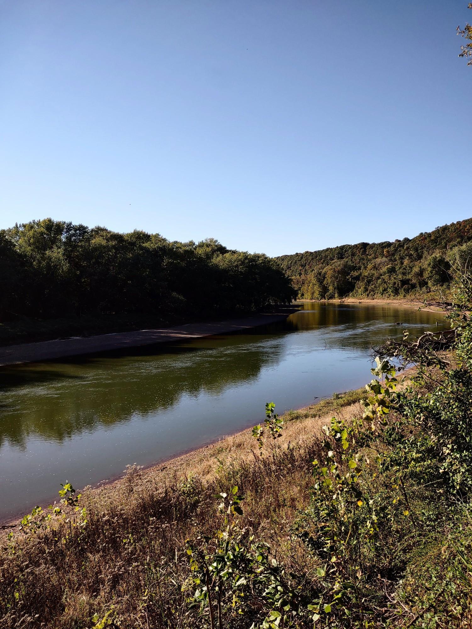 Calm river flowing between green banks under a clear, sunny sky.