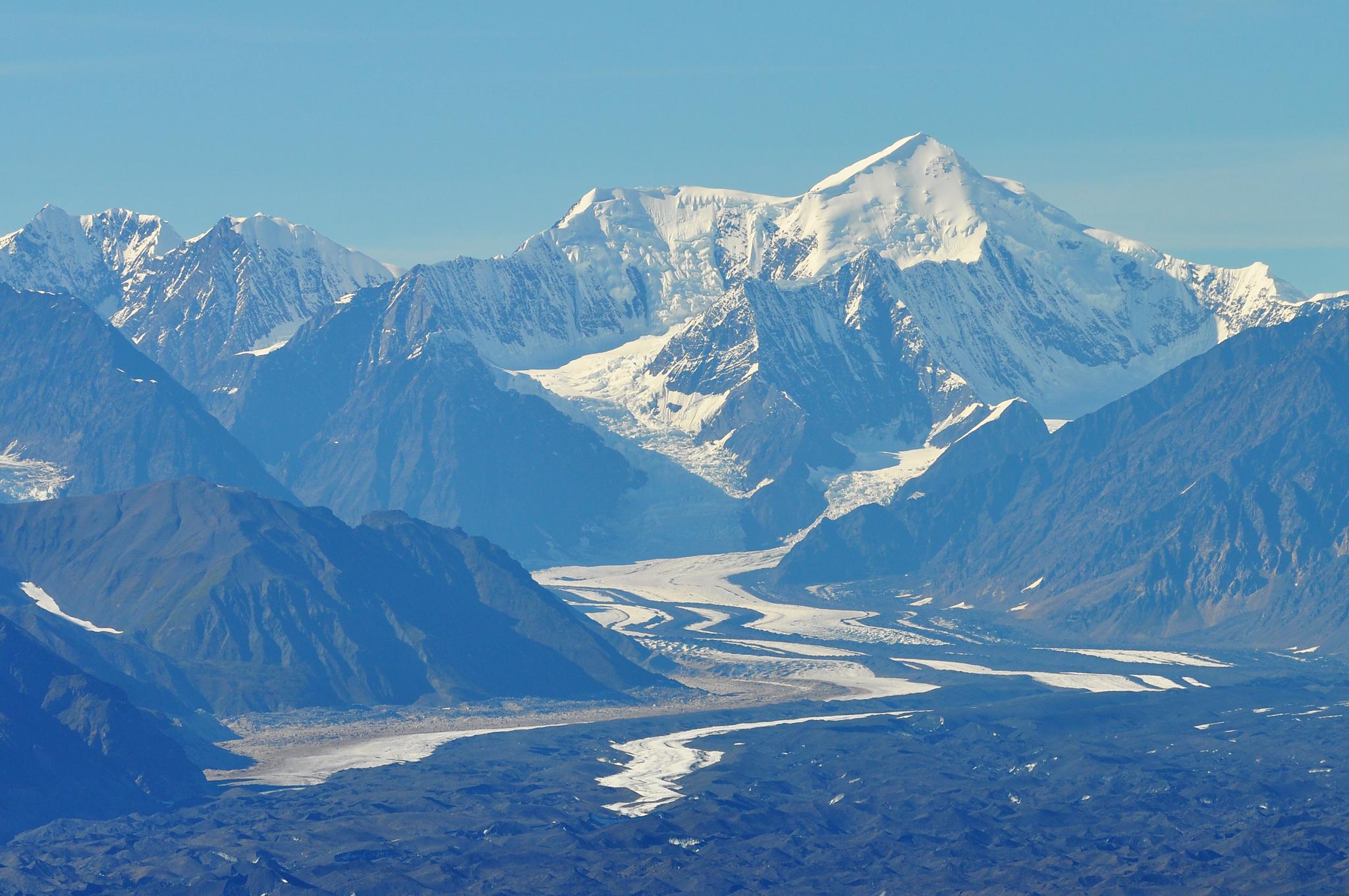 Majestic snow-capped mountains overlook a winding glacial valley under clear skies.