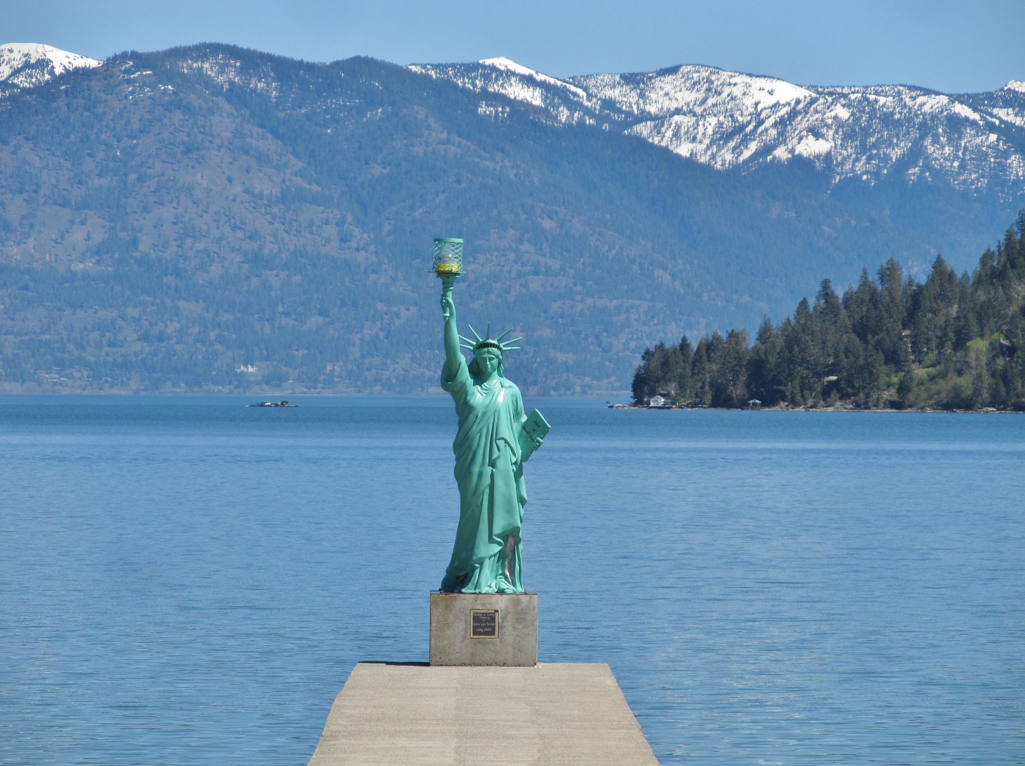 Statue of Liberty replica on a dock, calm water, forested mountains, bright day. - Popsicle Bridge loop from Sandpoint