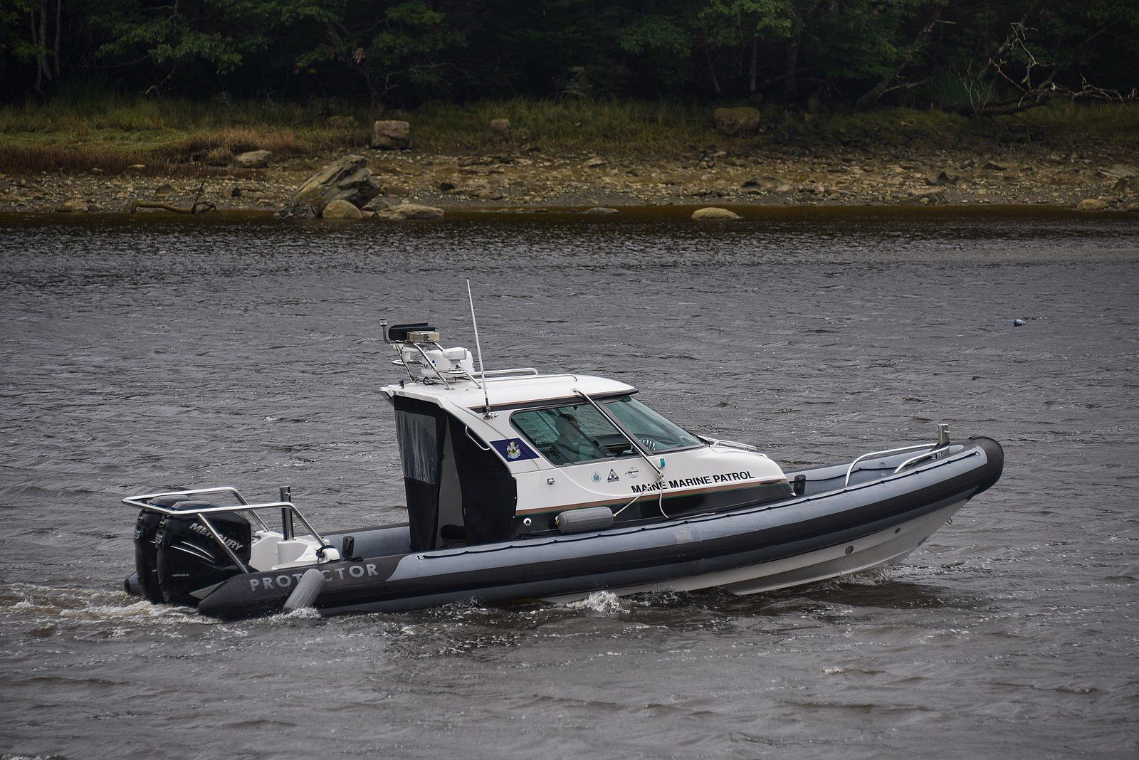 A white and grey patrol boat moves across dark water near a treeline. - Down East Sunrise Trail