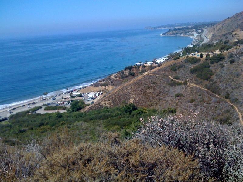 Panoramic view of a bright blue ocean, sandy beach, and dry coastal hills.