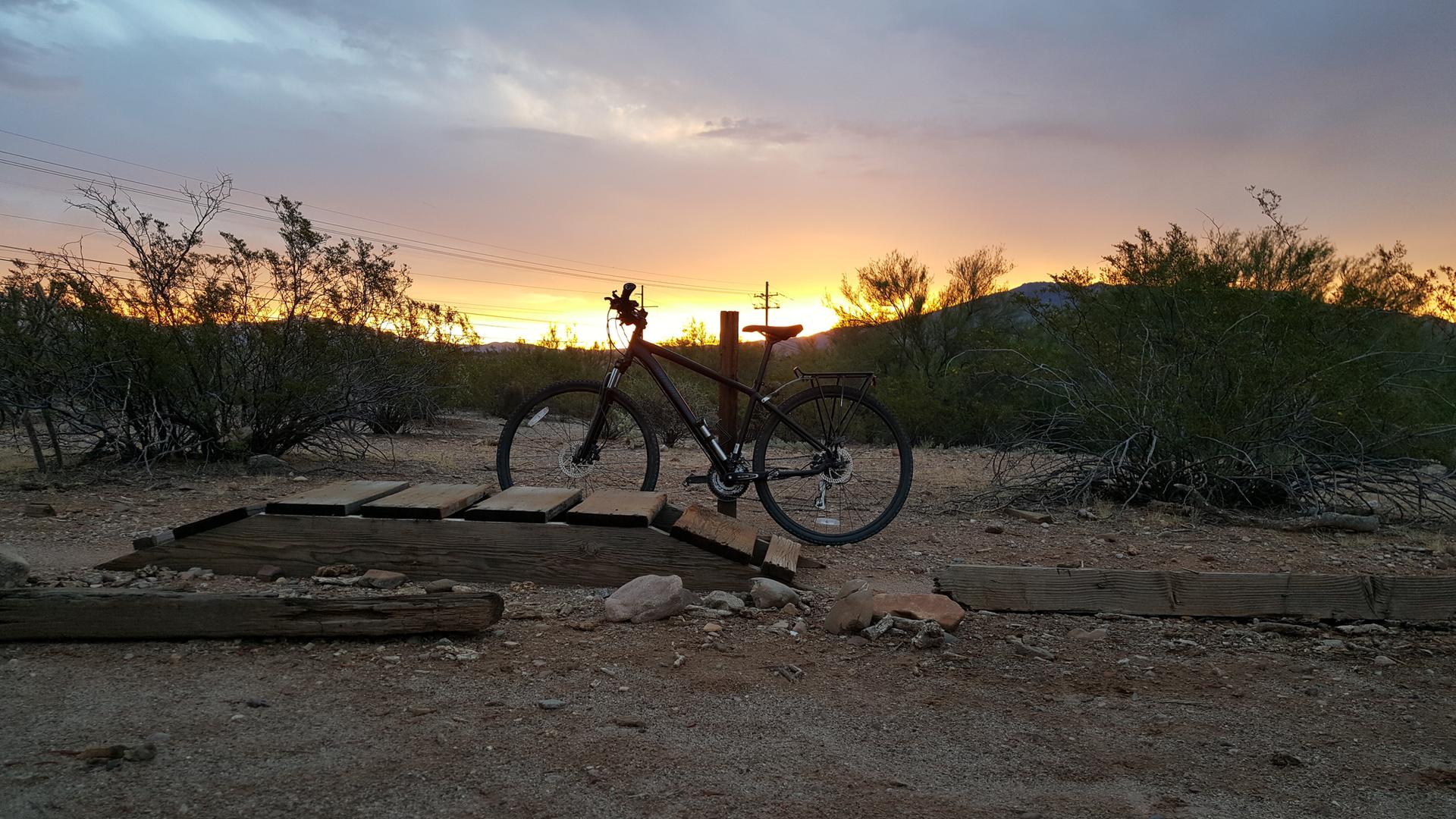 Mountain bike on a wooden ramp at sunset in a desert landscape.