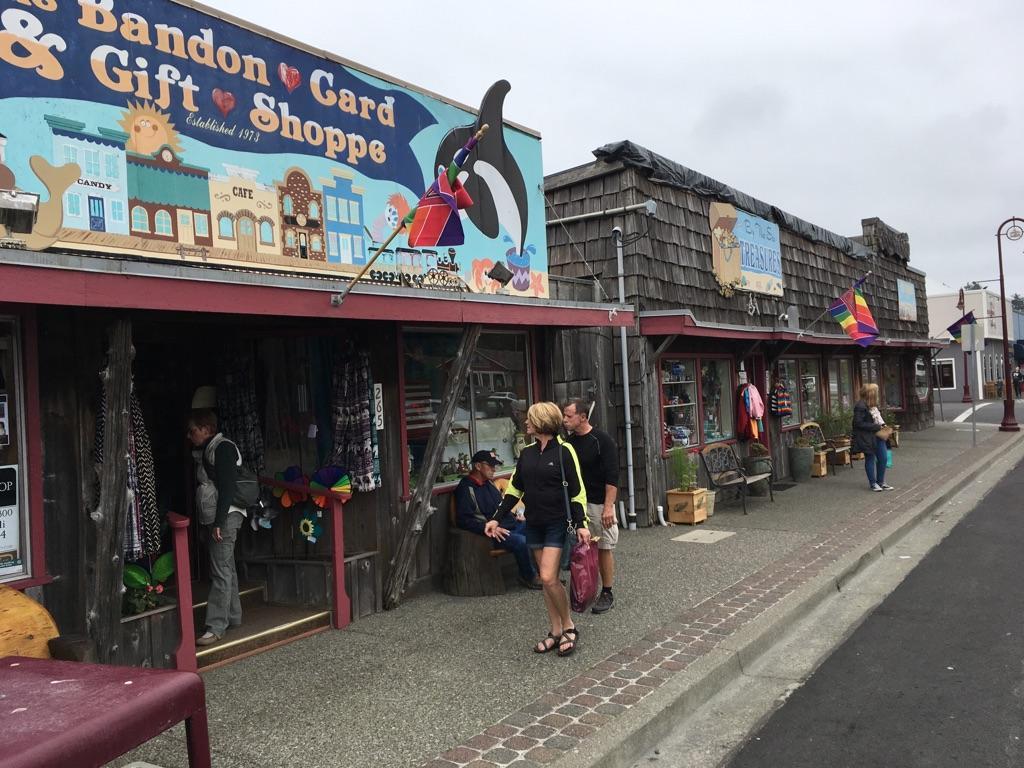 People walk past colorful storefronts on a cloudy day in a small town.
