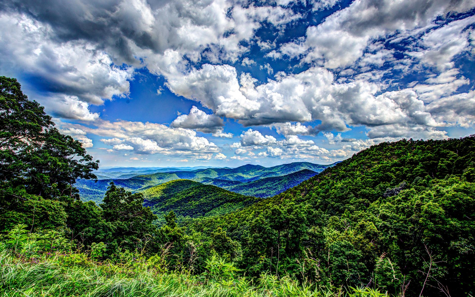 Vibrant green mountains under a dramatic blue sky with fluffy white clouds.