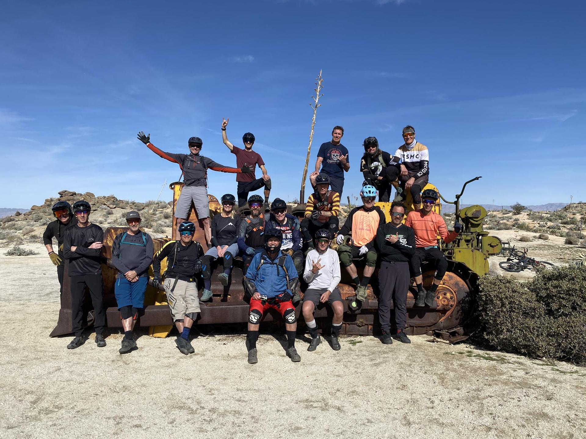 A large group of people posing on old machinery under a bright desert sky.