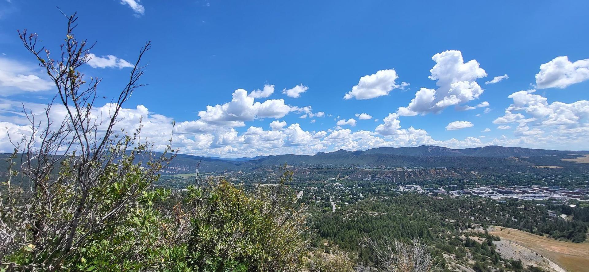 Expansive view of a valley with distant buildings under a bright blue sky.