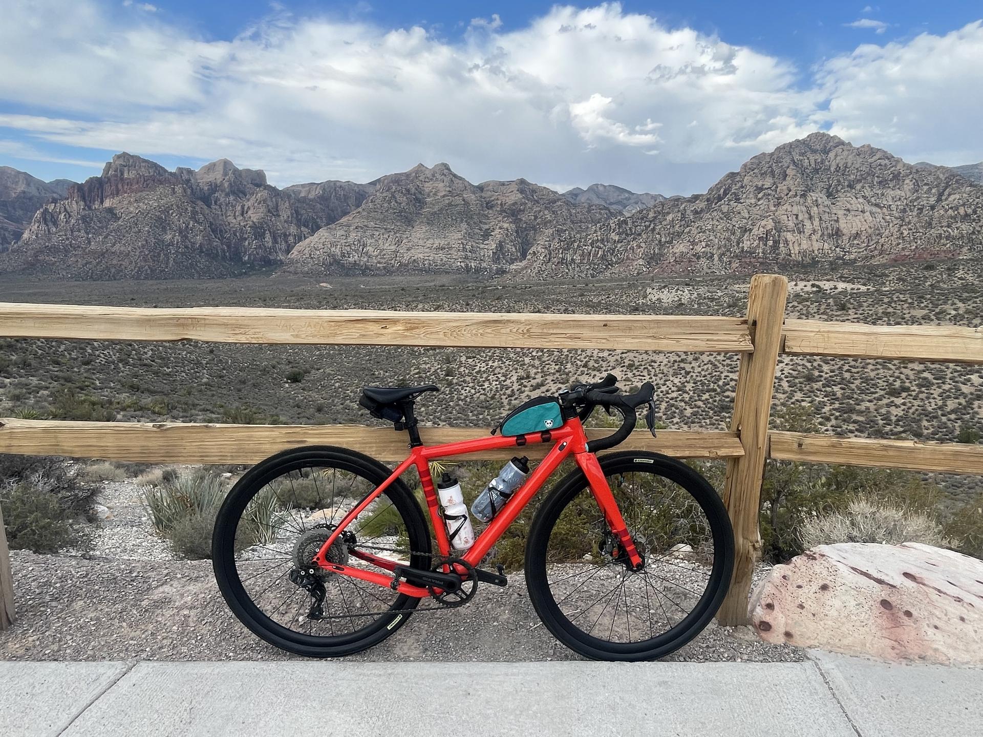 A red bicycle rests against a wooden fence with distant desert mountains.