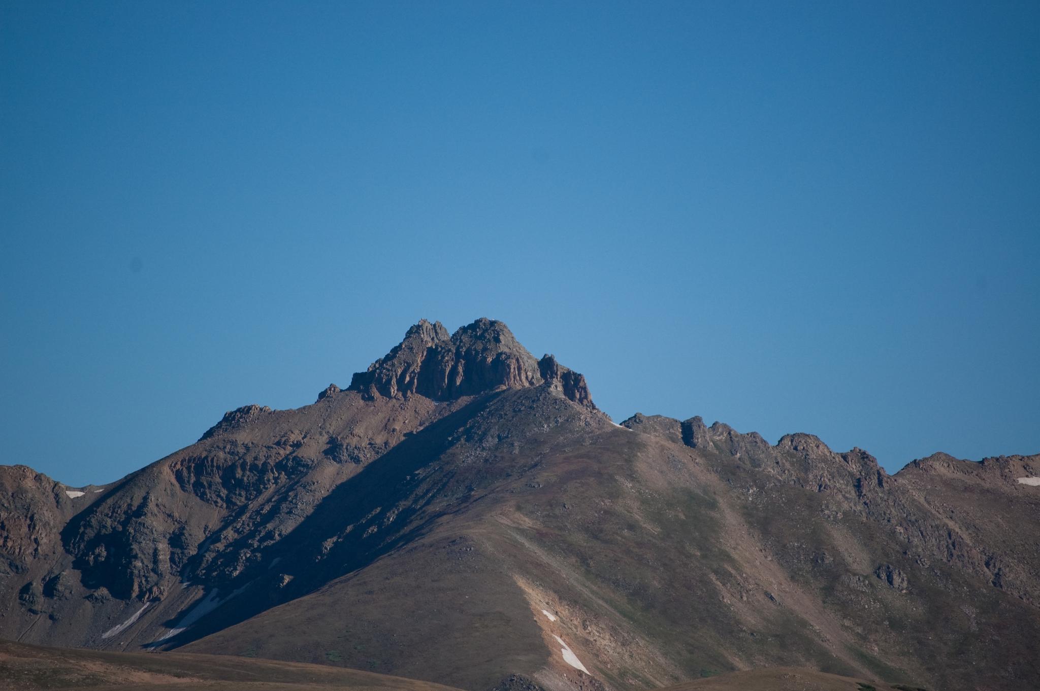 A rugged mountain peak stands tall against a clear blue sky.