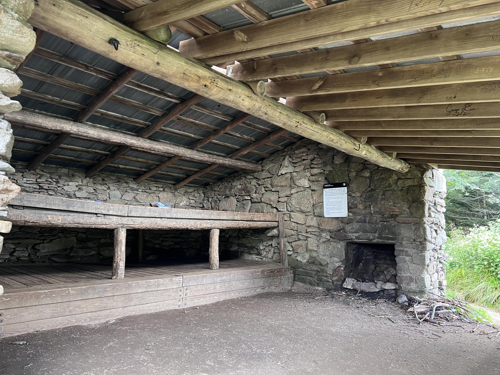 Rustic stone and wood shelter with a dirt floor and wooden bunks.