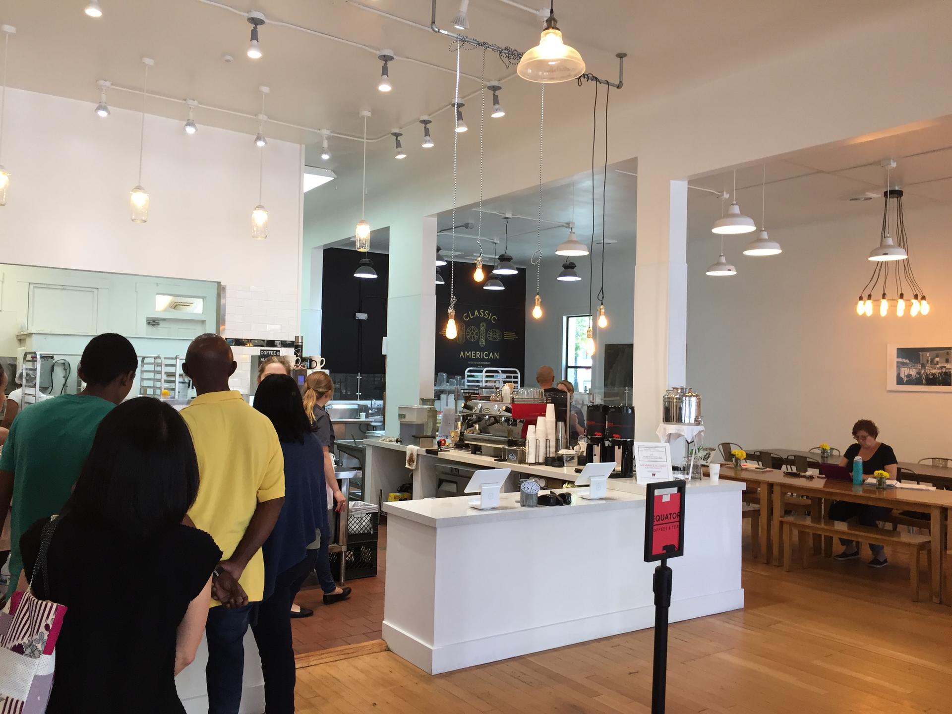 People waiting in line at a brightly lit indoor cafe.