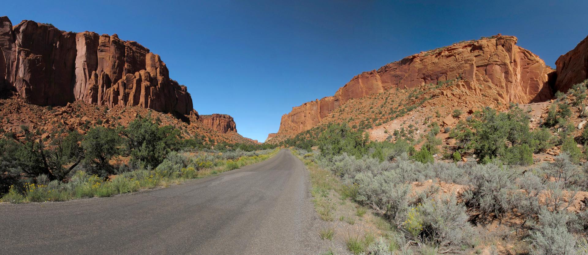 A paved road winds through a wide canyon under a clear blue sky.